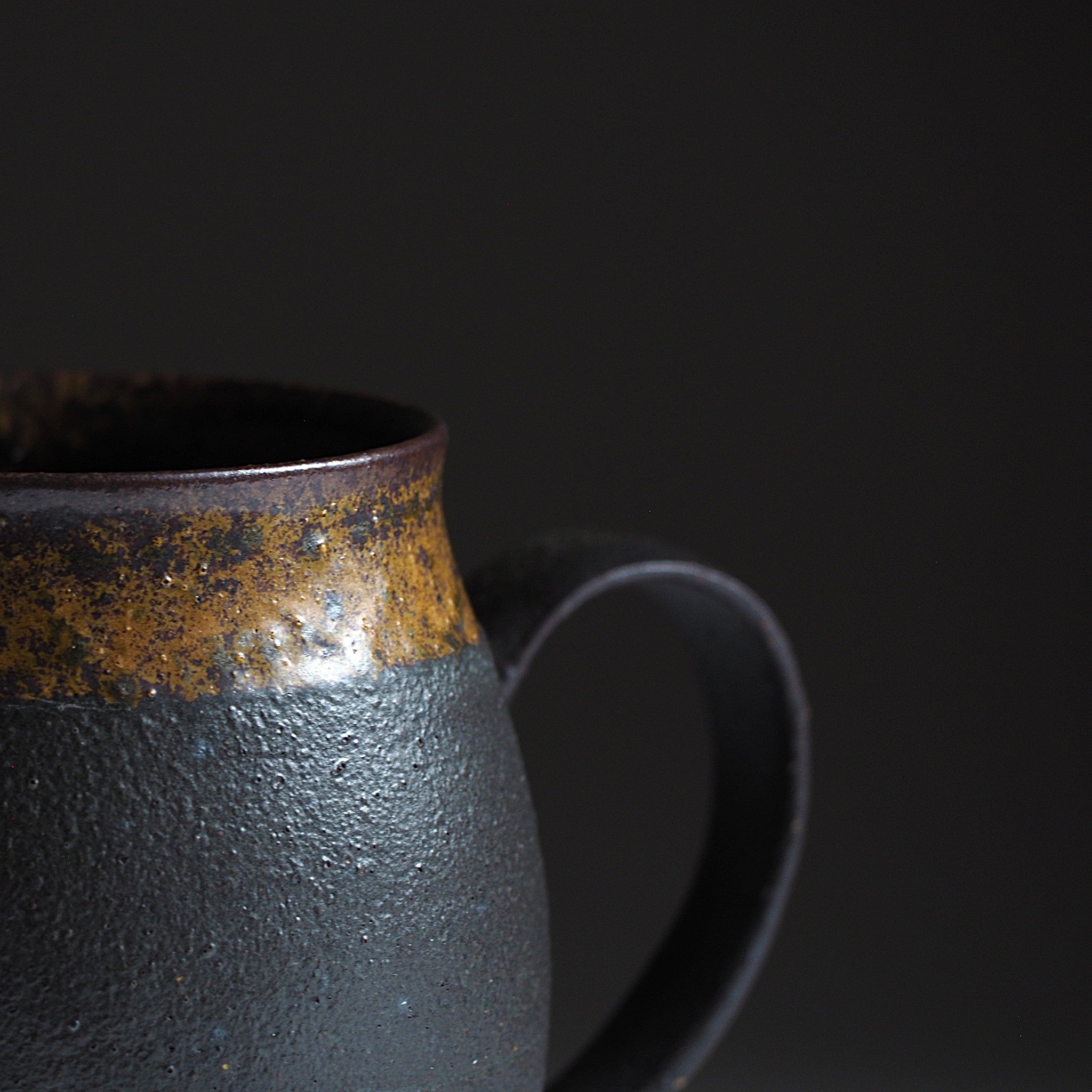 Close-up of handcrafted black Japanese ceramic tea mug on a dark background, Tsukushi