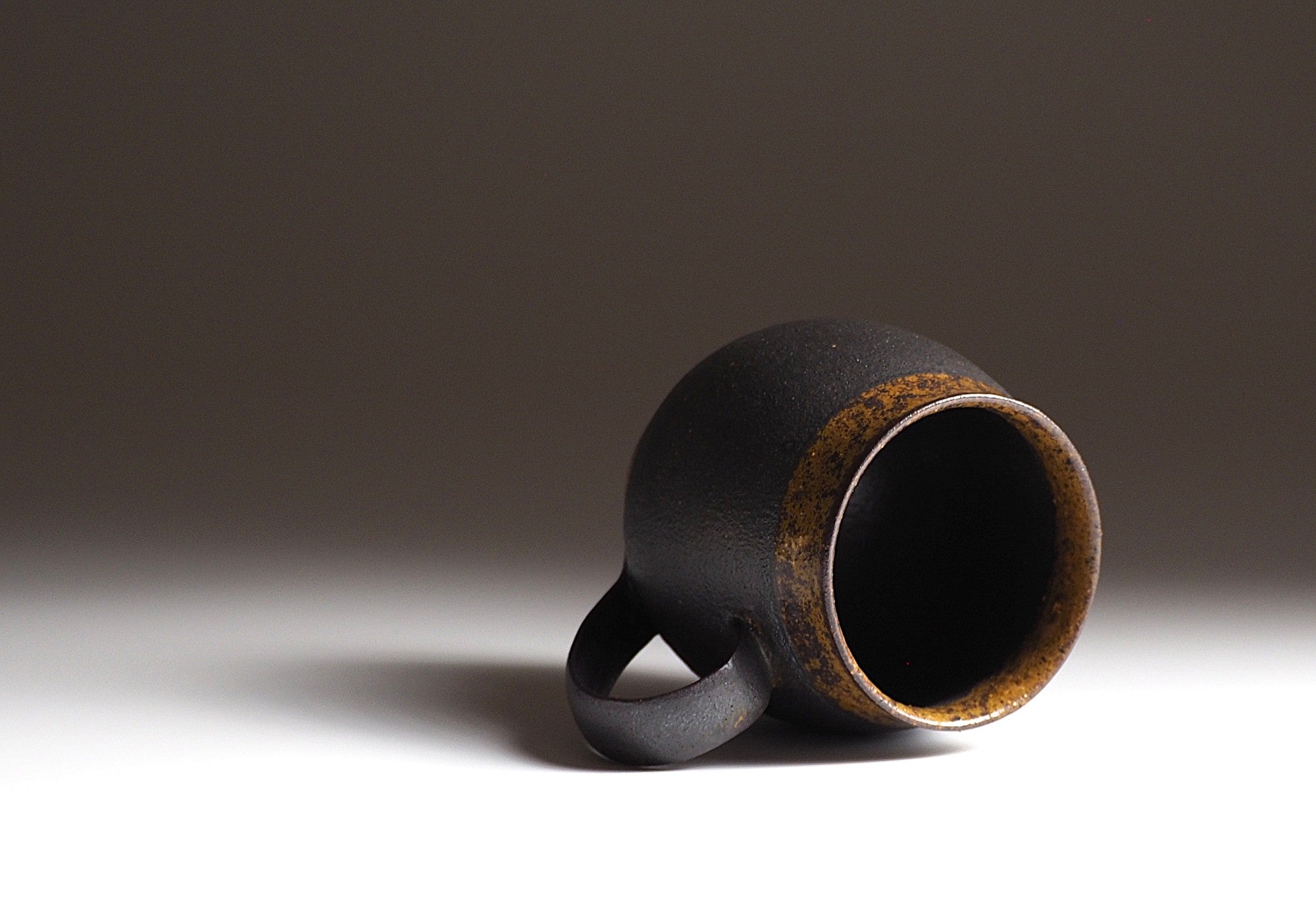 Handcrafted Japanese black ceramic tea mug with a rustic finish on a neutral background, Tsukushi