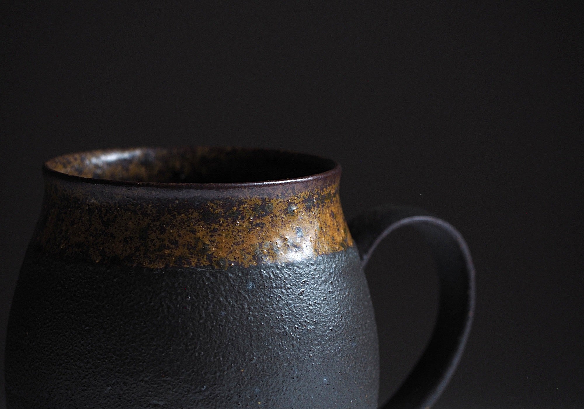 Detail of handcrafted black Japanese ceramic tea mug on a black background, Tsukushi