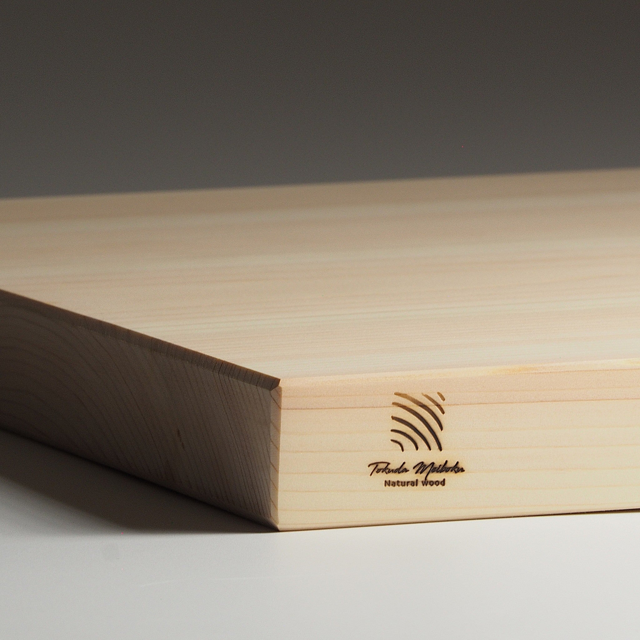Japanese wooden cutting board with a brand logo on a dark background. Tsukushi
