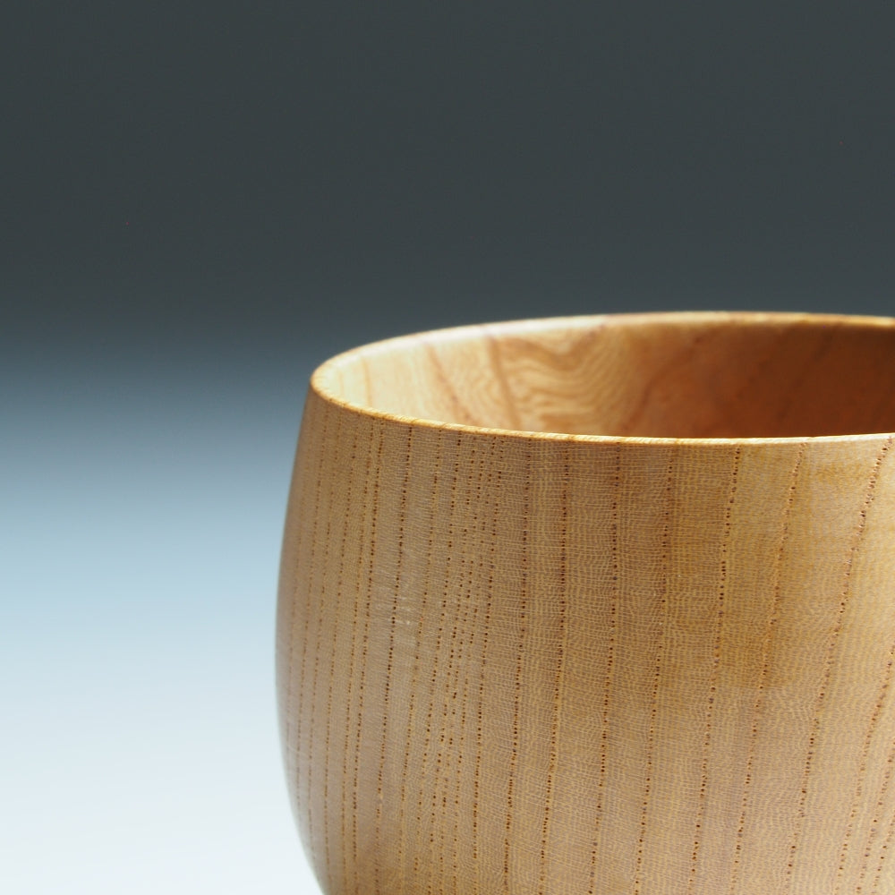 A close-up of a wooden cup on a gray background. Tsukushi