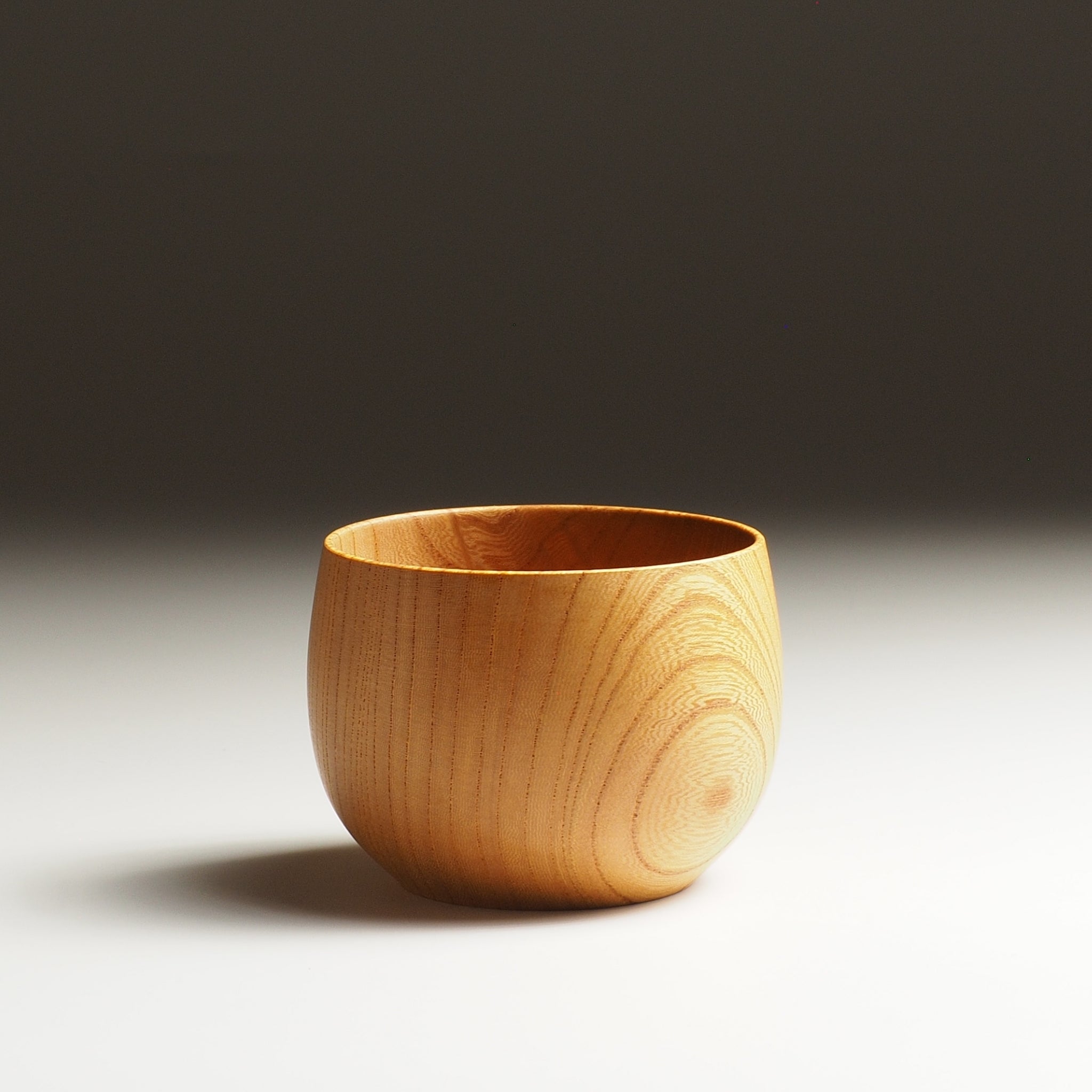 A Japanese wooden cup against a gradient background. Tsukushi