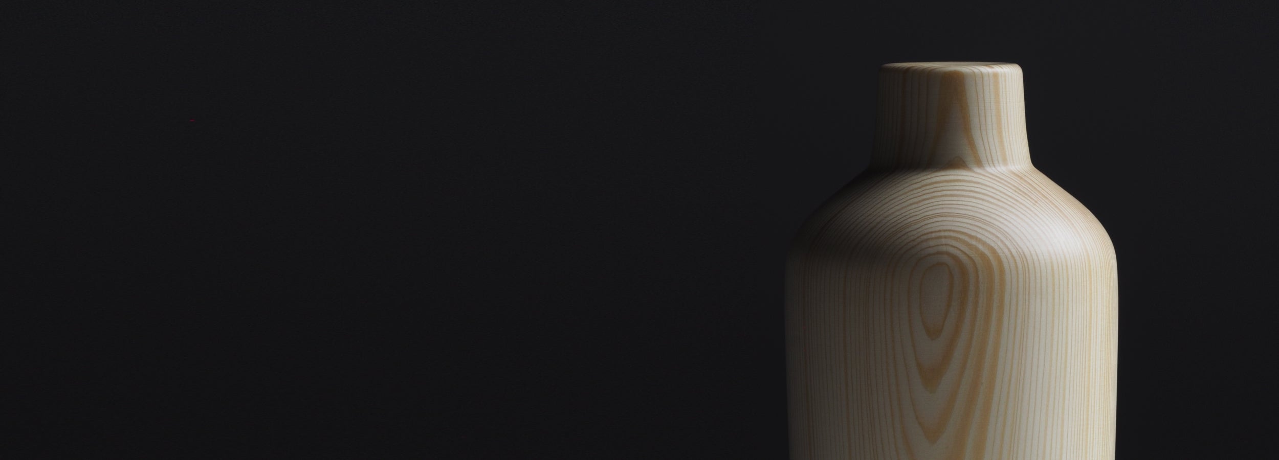 A Japanese wooden vase with a gradient shadow on a black background. Tsukushi