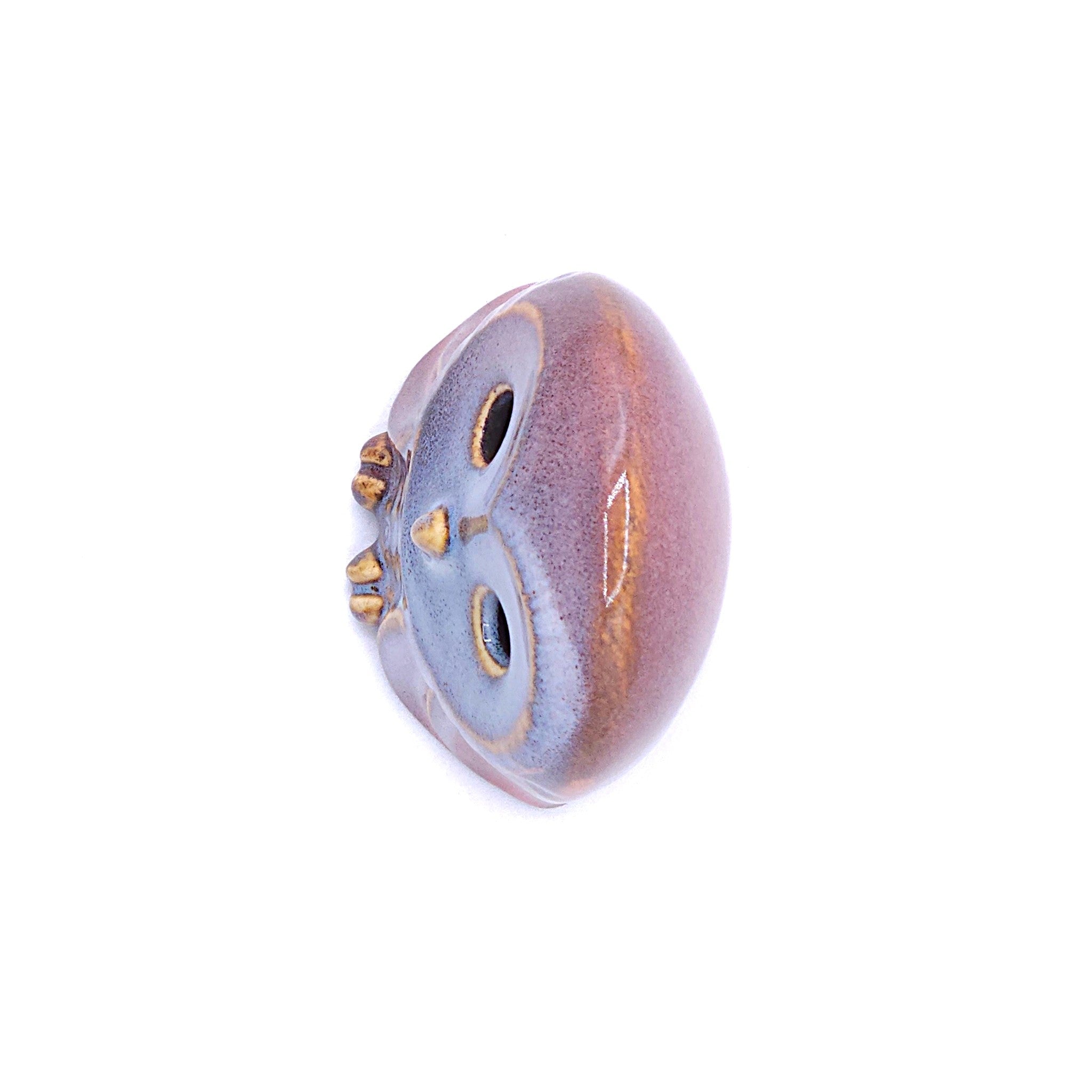 A top view of a handcrafted pottery figurine of an owl with a pink. Tsukushi