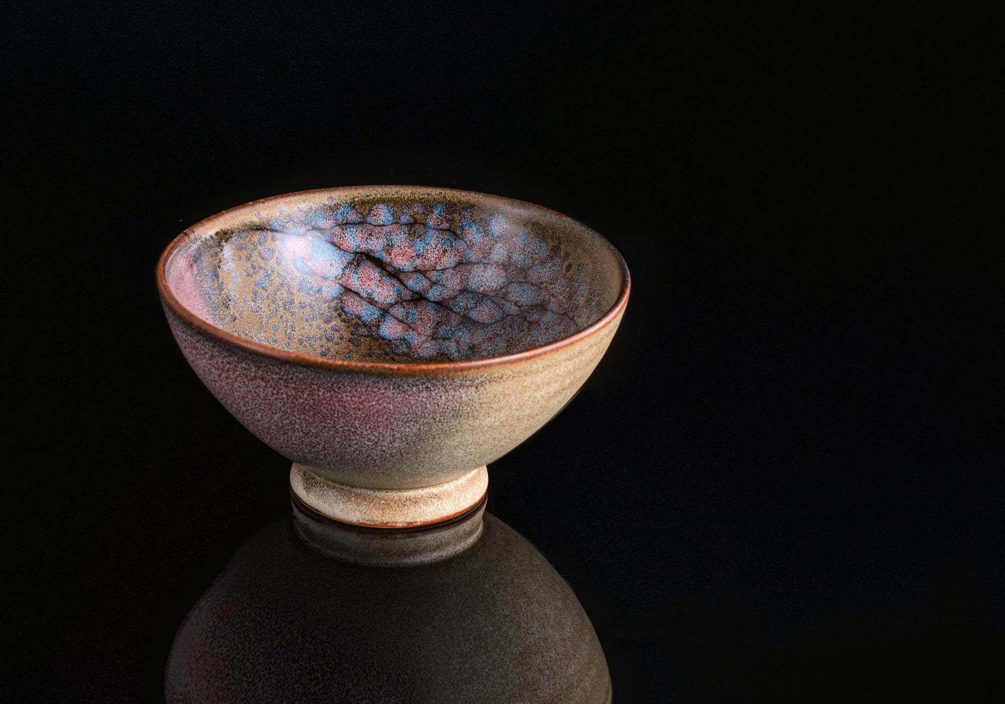 A pink Japanese rice bowl with a cherry blossom pattern on a black reflective surface. Tsukushi