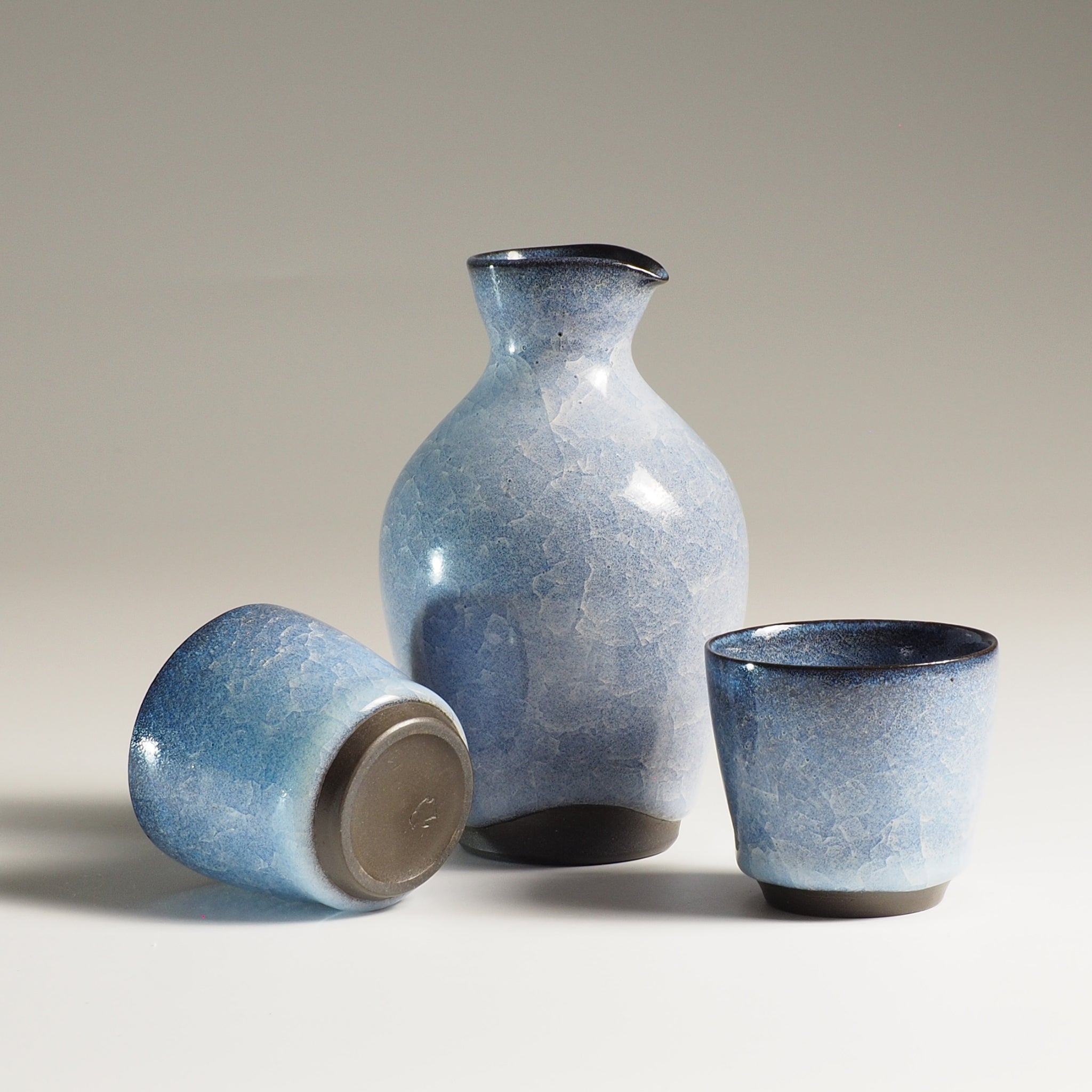Japanese handcrafted crazing ceramic Sake set (bottle and cups) beige background, Tsukushi