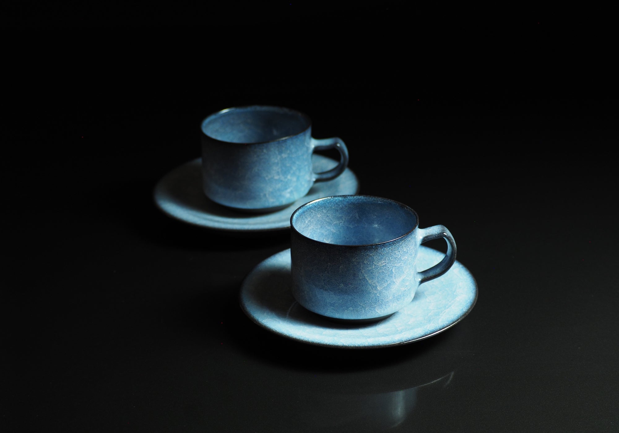 Handcrafted crazing Japanese ceramic coffee cups and saucers black background with reflection, Tsukushi