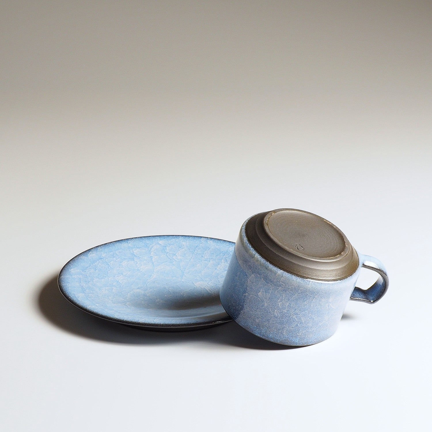 Handcrafted crazing Japanese ceramic coffee cup and saucer beige background from back, Tsukushi
