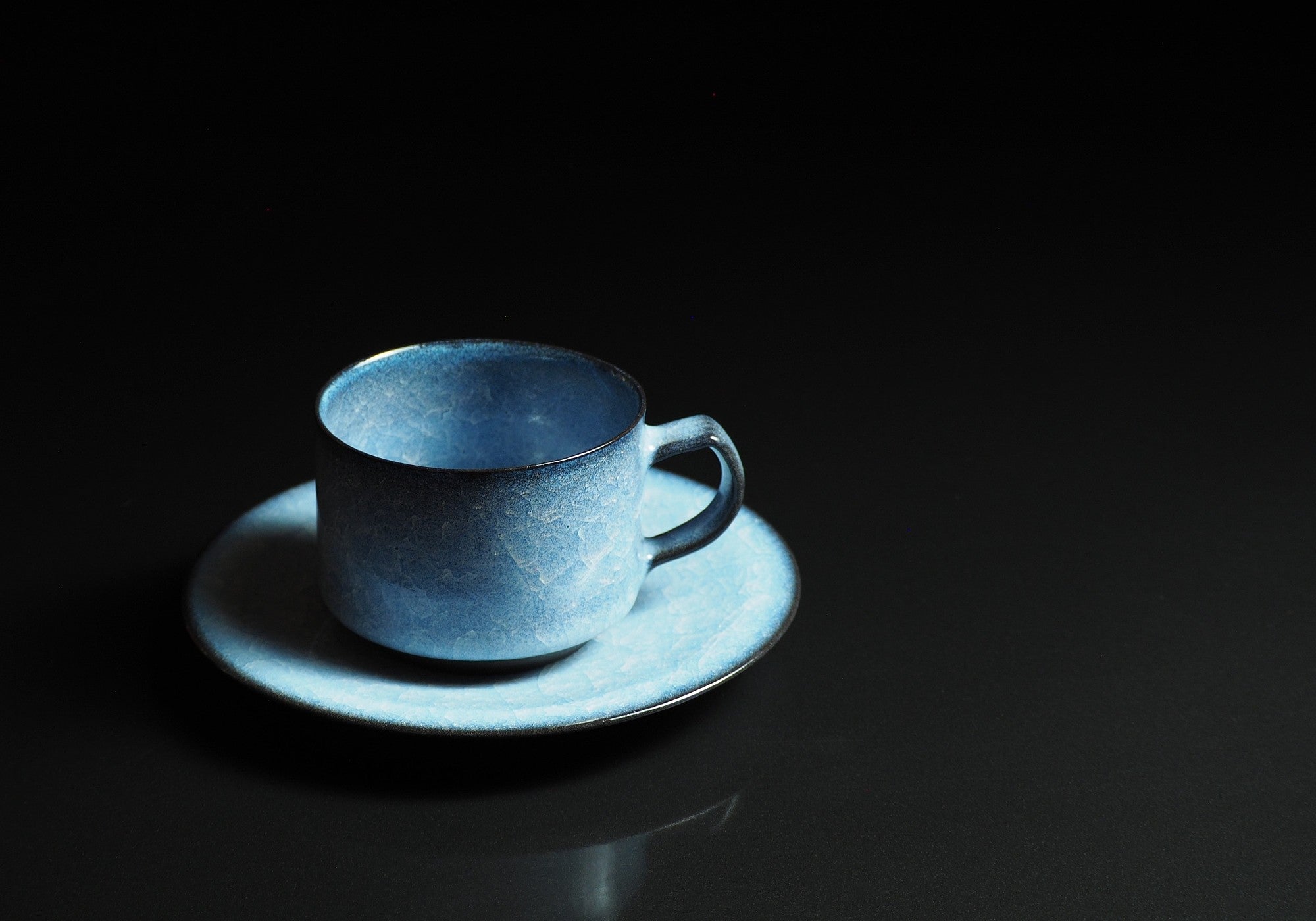 Handcrafted crazing Japanese ceramic coffee cup and saucer black background, Tsukushi