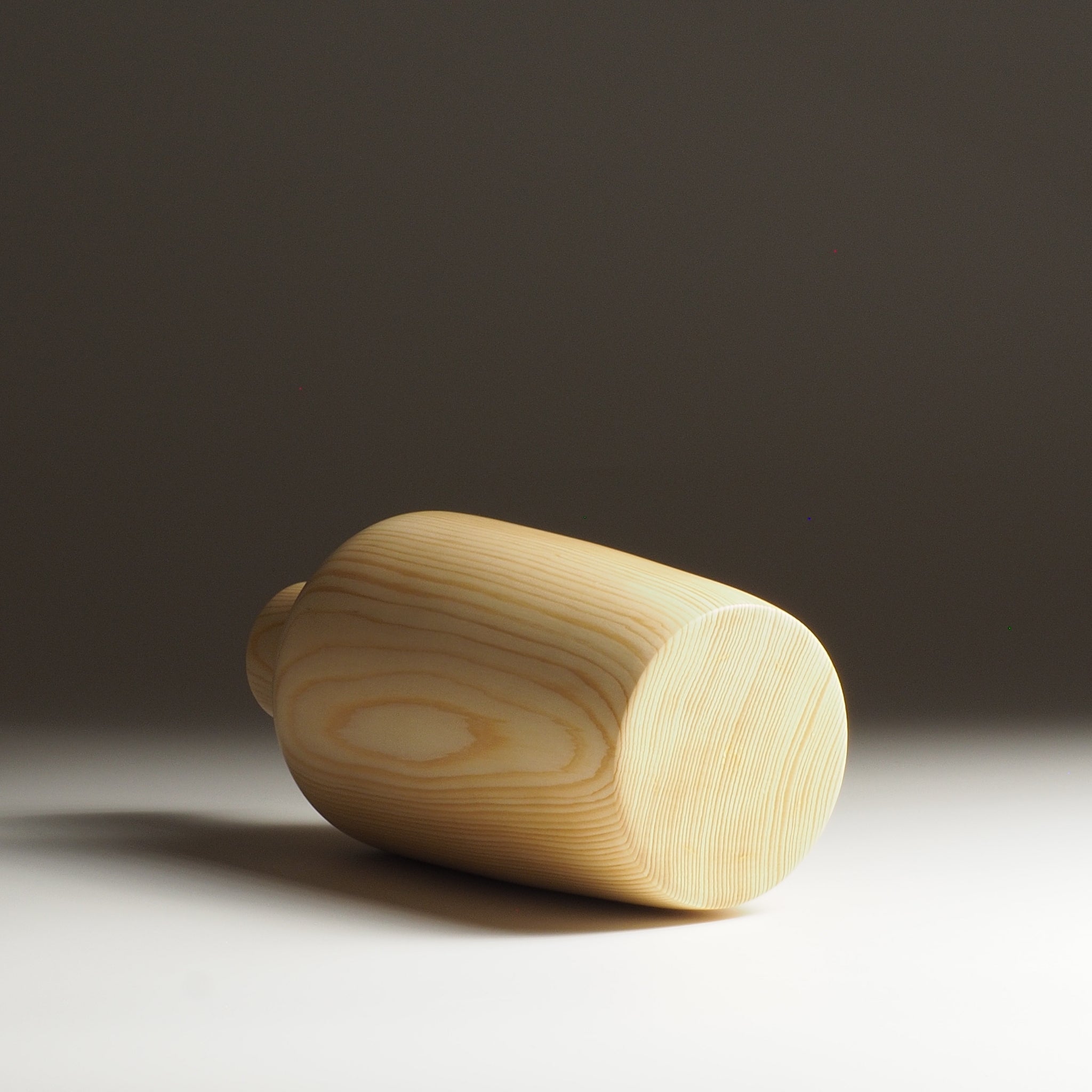A backside view of a Japanese wooden vase on a beige gradient background. Tsukushi