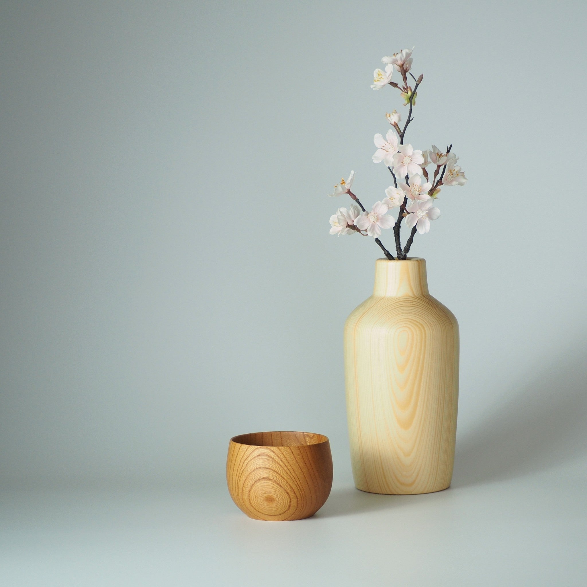 Wooden vase with floral arrangement and wooden cup on a light gray background | Tsukushi