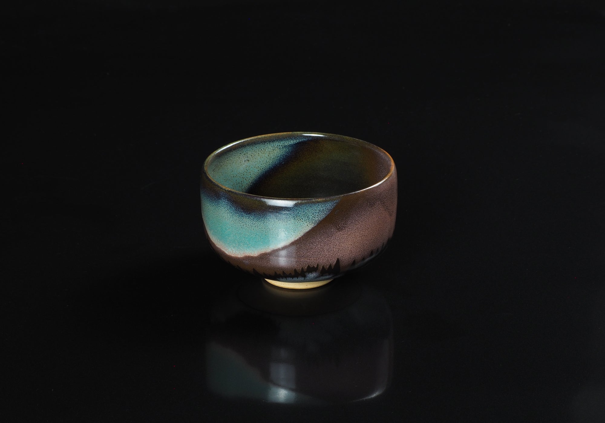 A Japanese ceramic matcha bowl designed with an Aurora against a black background. Tsukushi