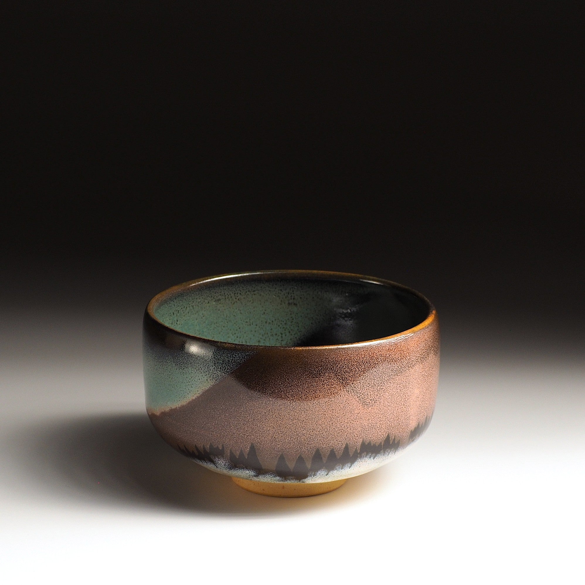 A Japanese ceramic matcha bowl adorned with a pink Aurora and a grove of trees against a black background. Tsukushi