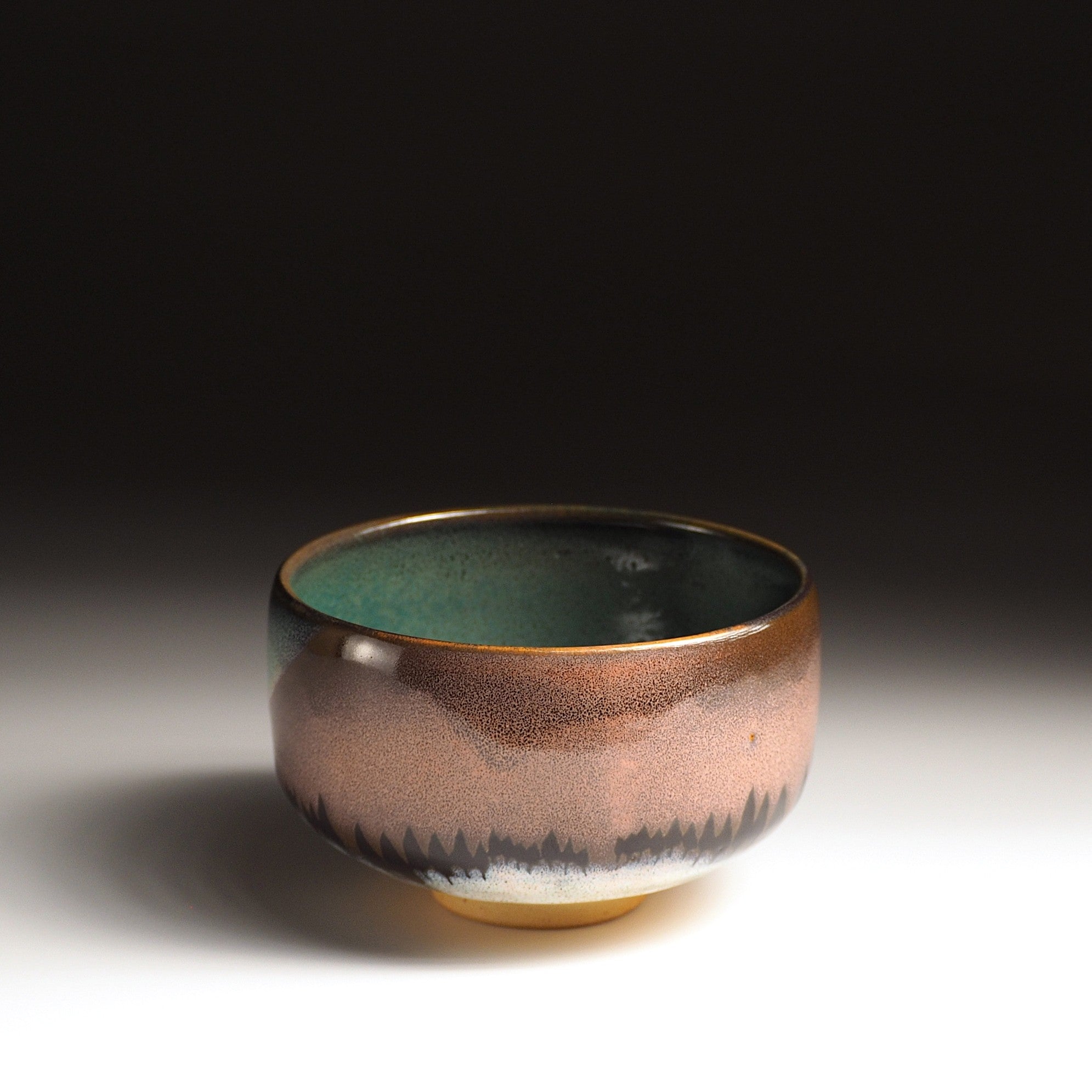 A Japanese ceramic matcha bowl designed with an aurora and grove of trees, set against a black background. Tsukushi