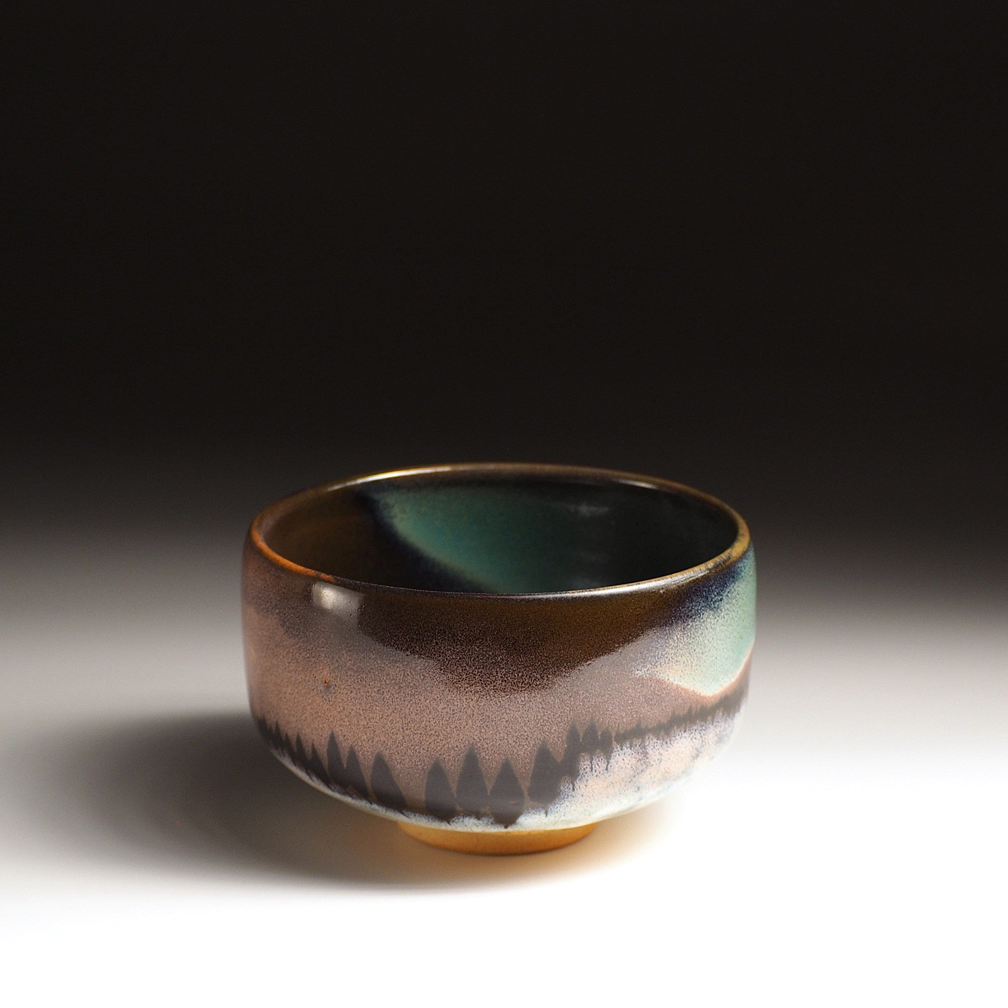 A Japanese ceramic matcha bowl adorned with an aurora and a bunch of trees against a black background. Tsukushi