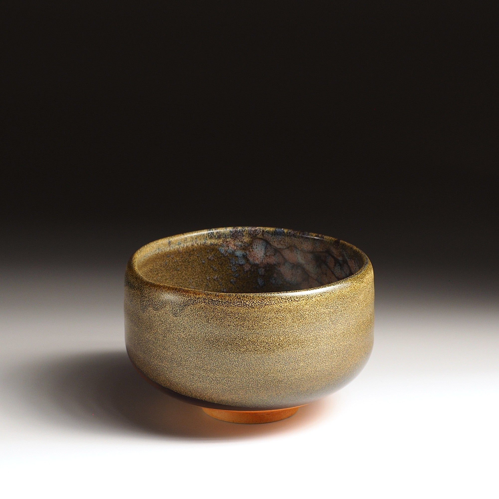 A Japanese ceramic matcha bowl adorned with cherry blossoms on a brown surface, set against a black background. Tsukushi.
