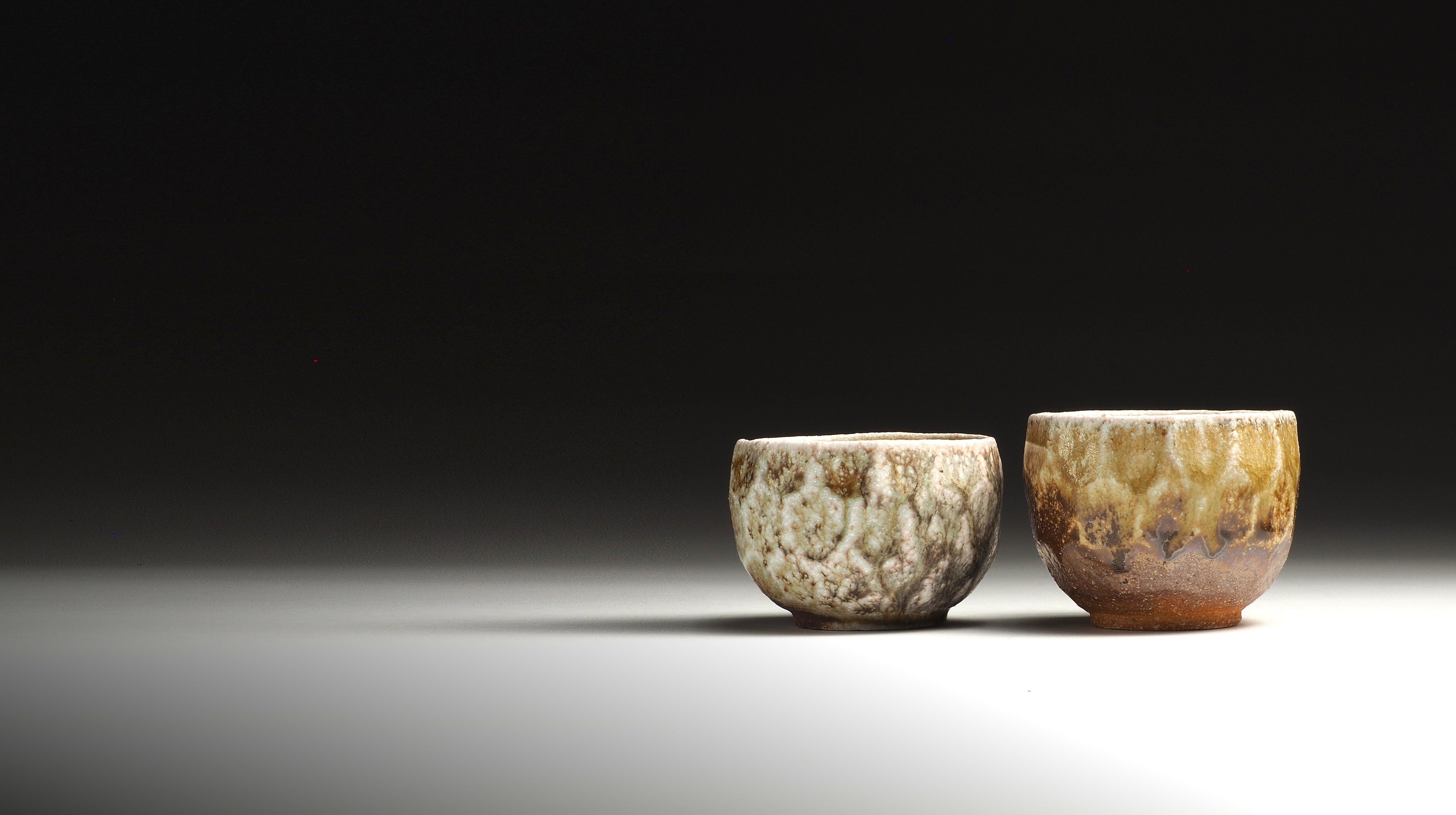 Two handmade Japanese Yakishime cups from Shigaraki with textured, mottled glazes in earthy tones of brown, beige, and muted gold