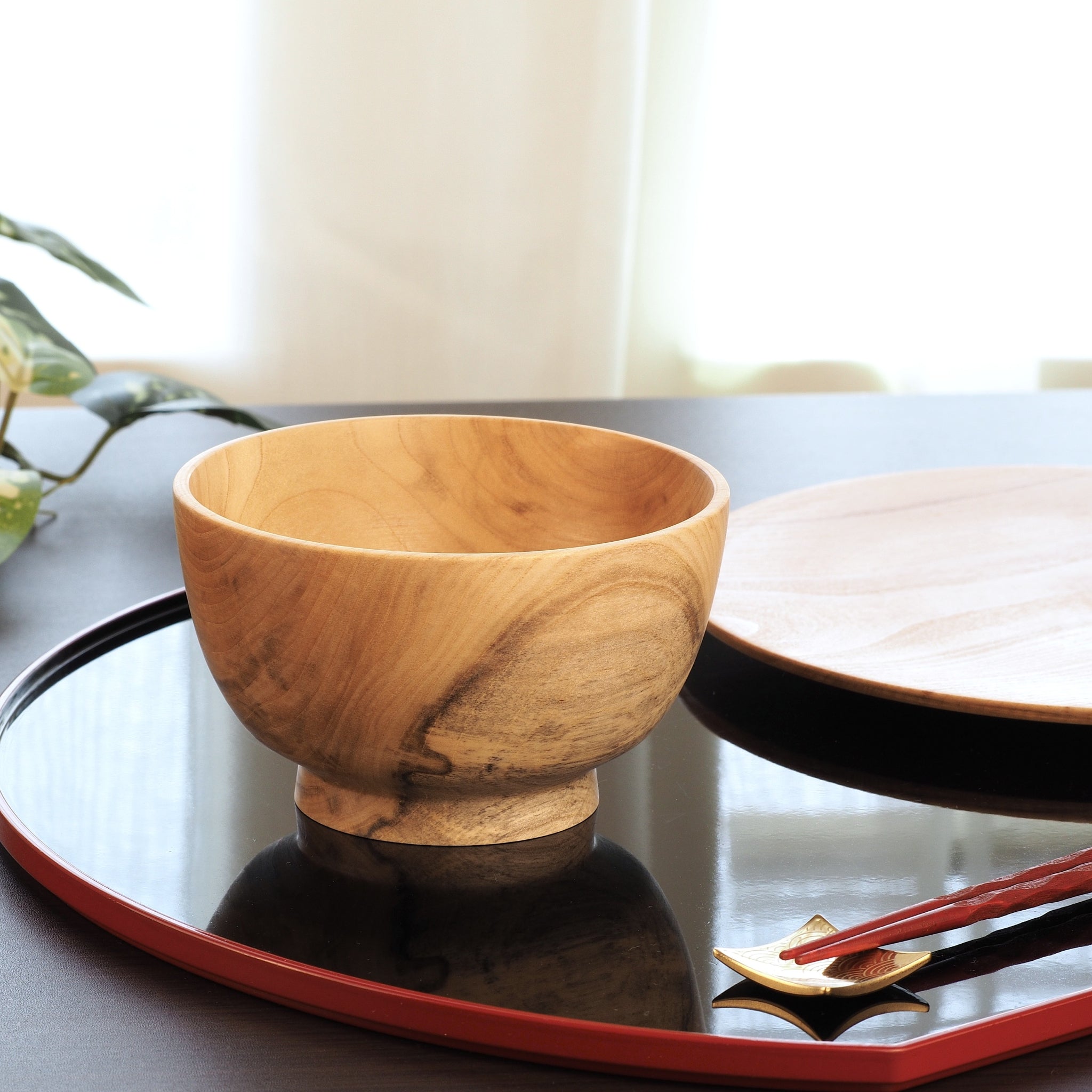 A wooden bowl on a reflective surface with a blurred background. Tsukushi