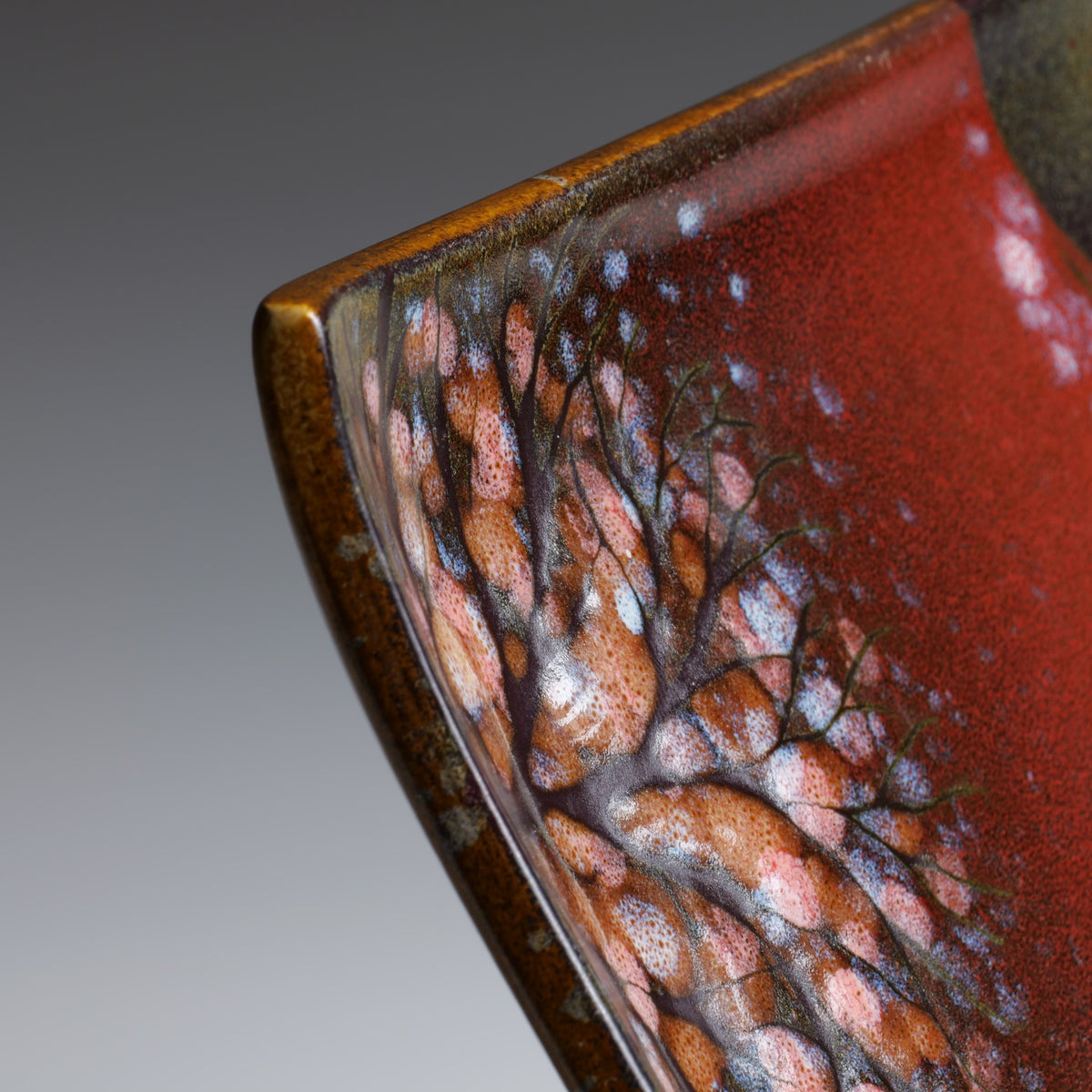 Macro detail of the Akafuji Japanese plate, highlighting the textured sakura tree pattern, reddish glaze, and intricate ceramic surface.