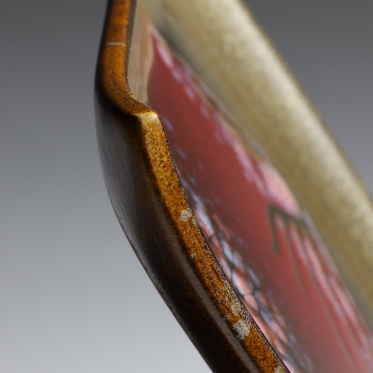 Side close-up of the Akafuji square ceramic plate showing its gently curved rim, ceramic thickness, and layered glaze finish.