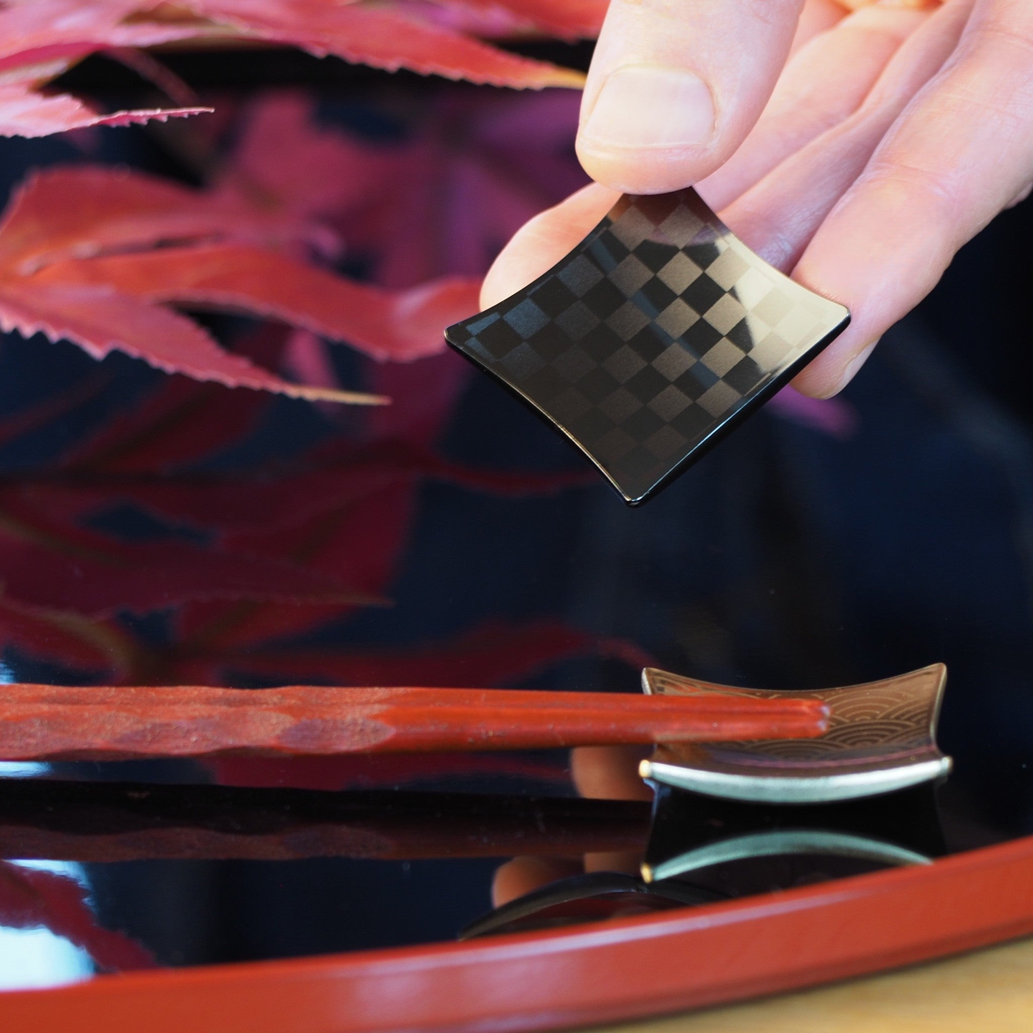 Hand holding a black chopstick rest over a reflective surface. Tsukushi