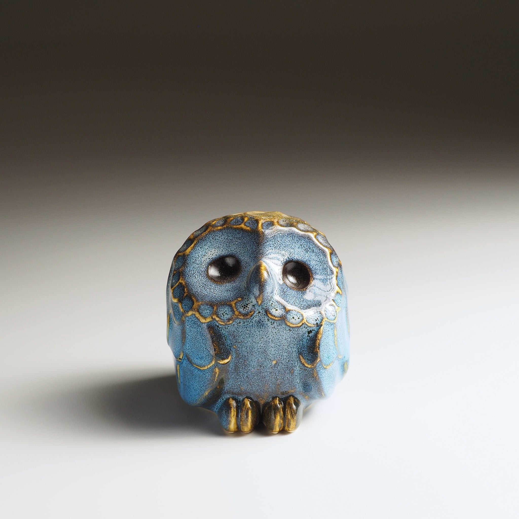 Front view of the small Fukumori ceramic owl ornament with large dark eyes and blue-and-gold glaze