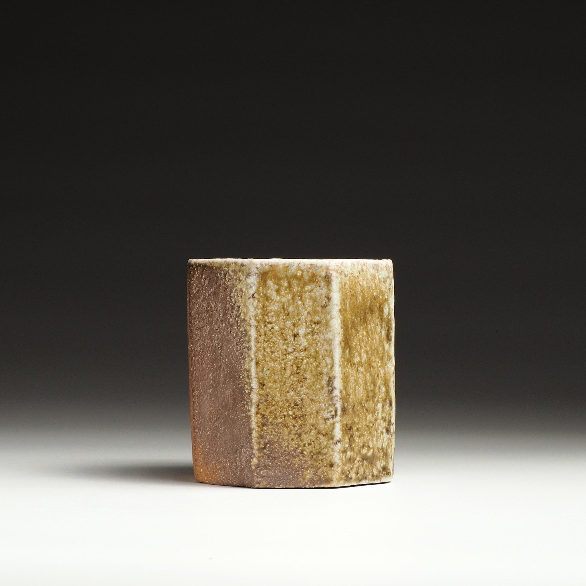 Side view of a Hachiryō handmade Shigaraki cup showing a textured beige and brown faceted surface.