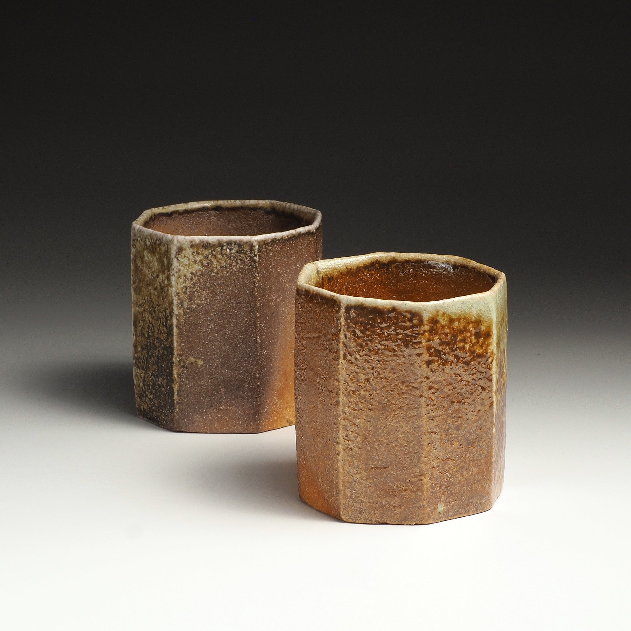 Two cups of the Hachiryō handmade Shigaraki set arranged together, showing their octagonal forms and earthy brown surfaces.