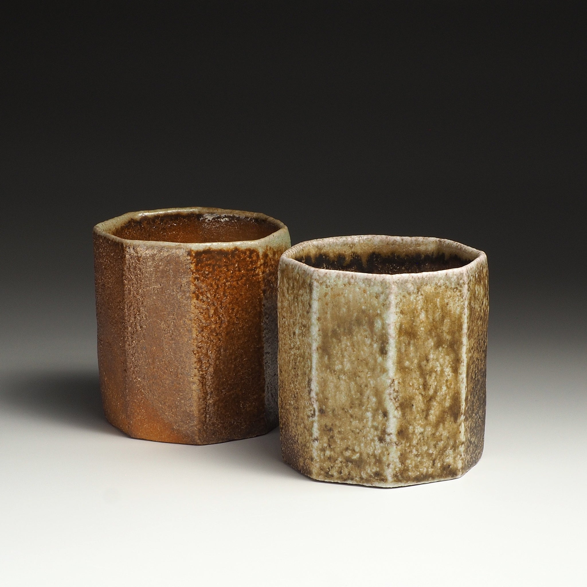 Two handmade cups of the Hachiryō Shigaraki set standing side by side with contrasting brown and beige firing tones.