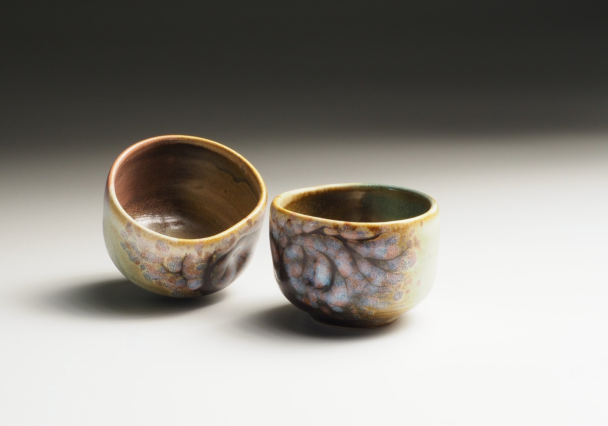Two ceramic guinomi cups with sakura design on a neutral background