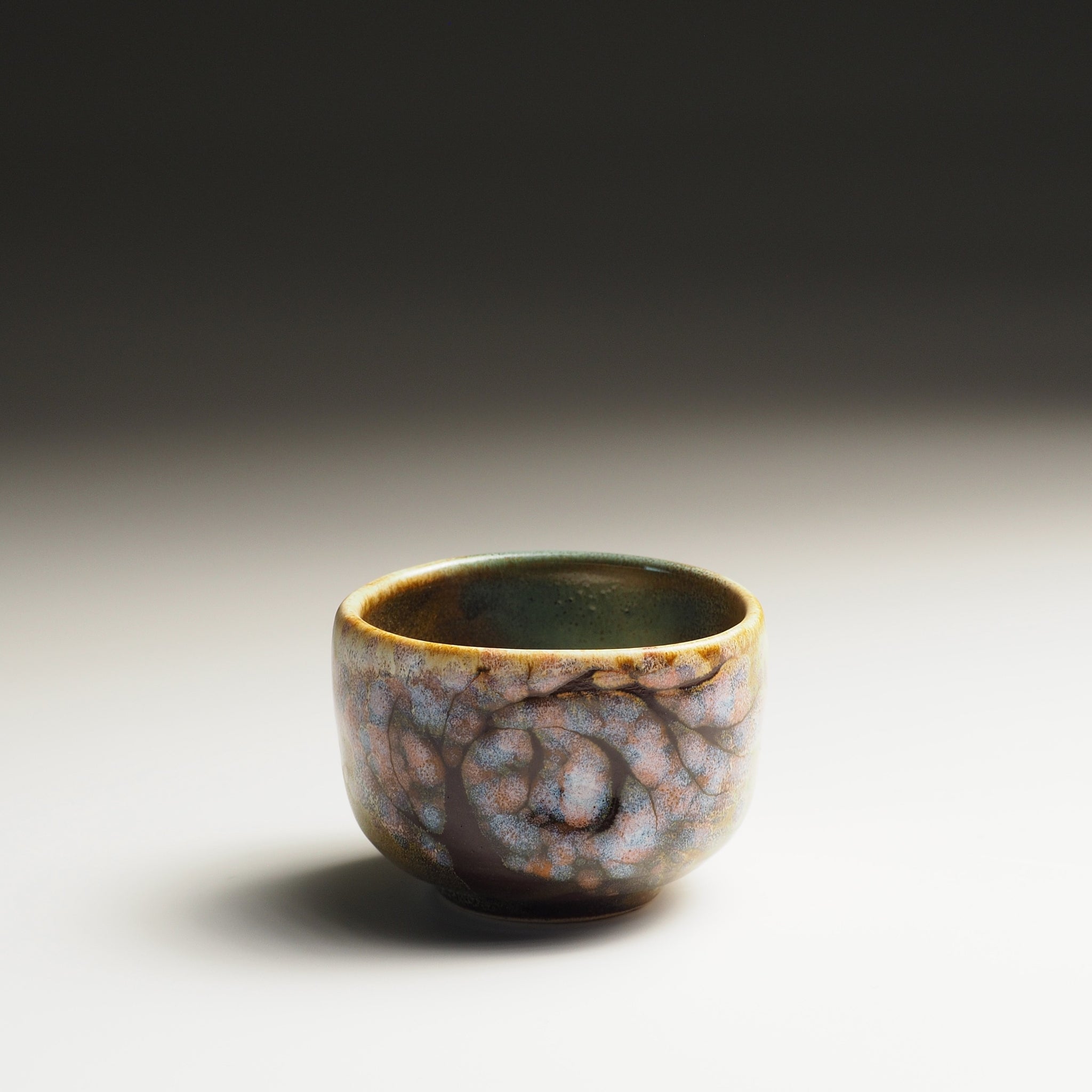 Ceramic guinomi sake cup with sakura design on a gradient background