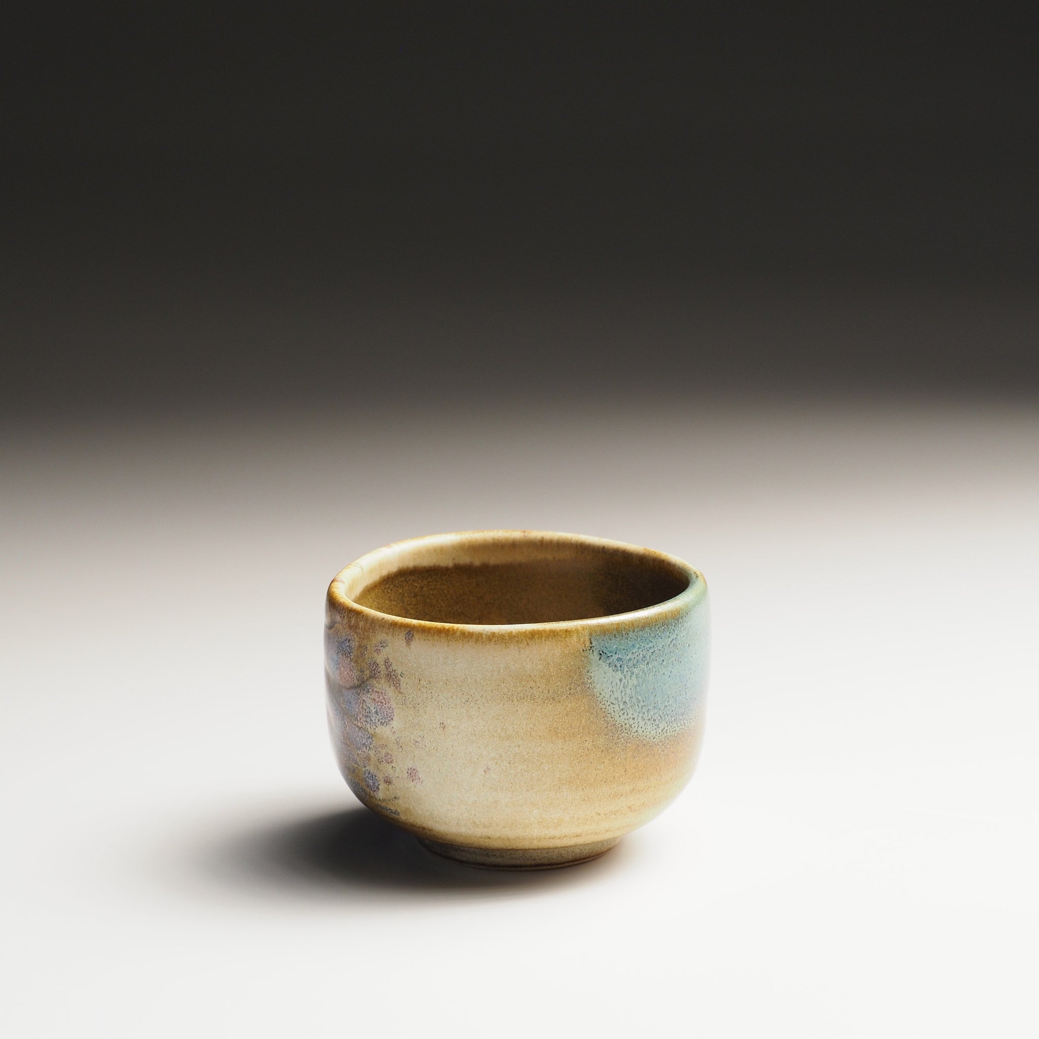 Pottery guinomi sake cup with sakura decorations on a gradient background