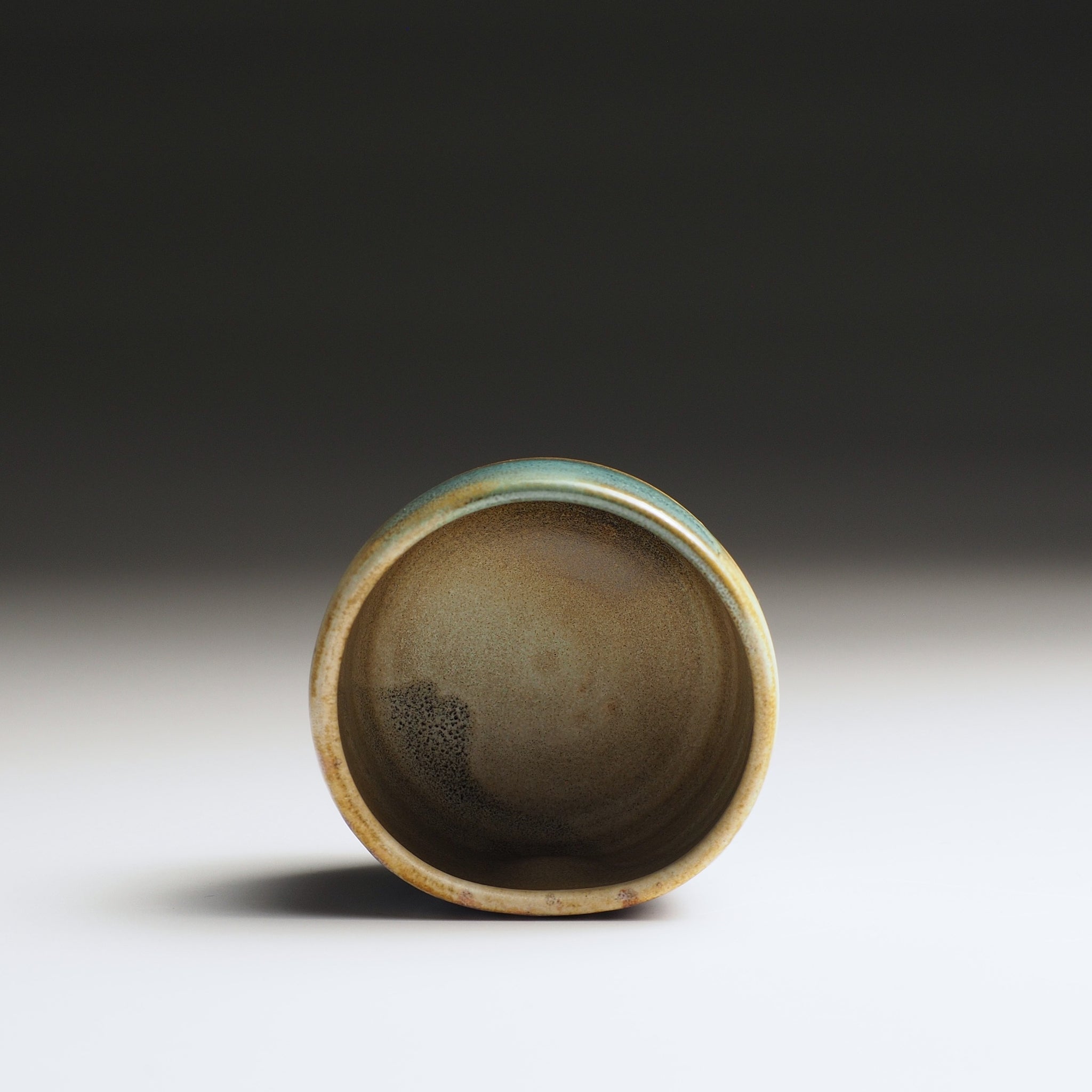 Close-up of the interior of a guinomi sake cup with a textured interior on a gradient background