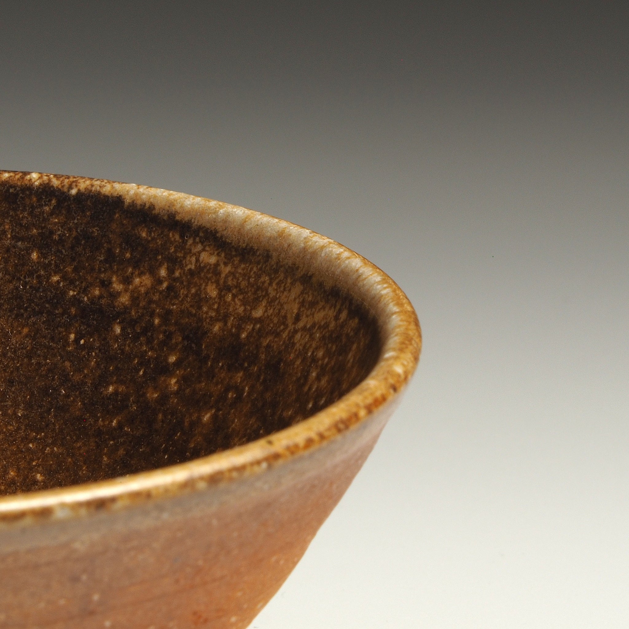 Close-up of a Mizuho handmade Shigaraki rice bowl showing its dark brown interior, softly mottled glaze, and rounded rim.