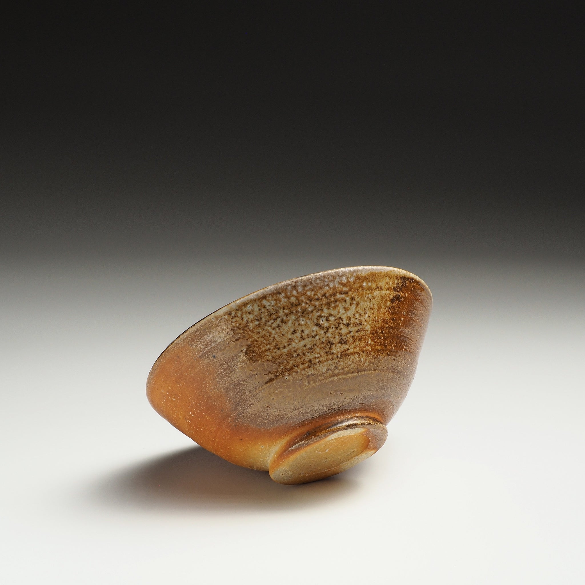 Mizuho handmade Shigaraki rice bowl resting on its side, showing the foot ring and mottled beige-brown ash-fired surface.