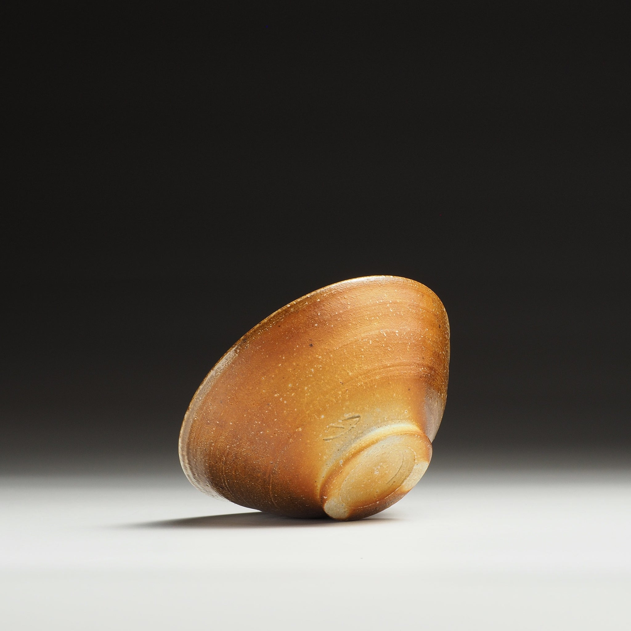 Mizuho Shigaraki rice bowl turned on its side, showing the base and warm amber firing tones.
