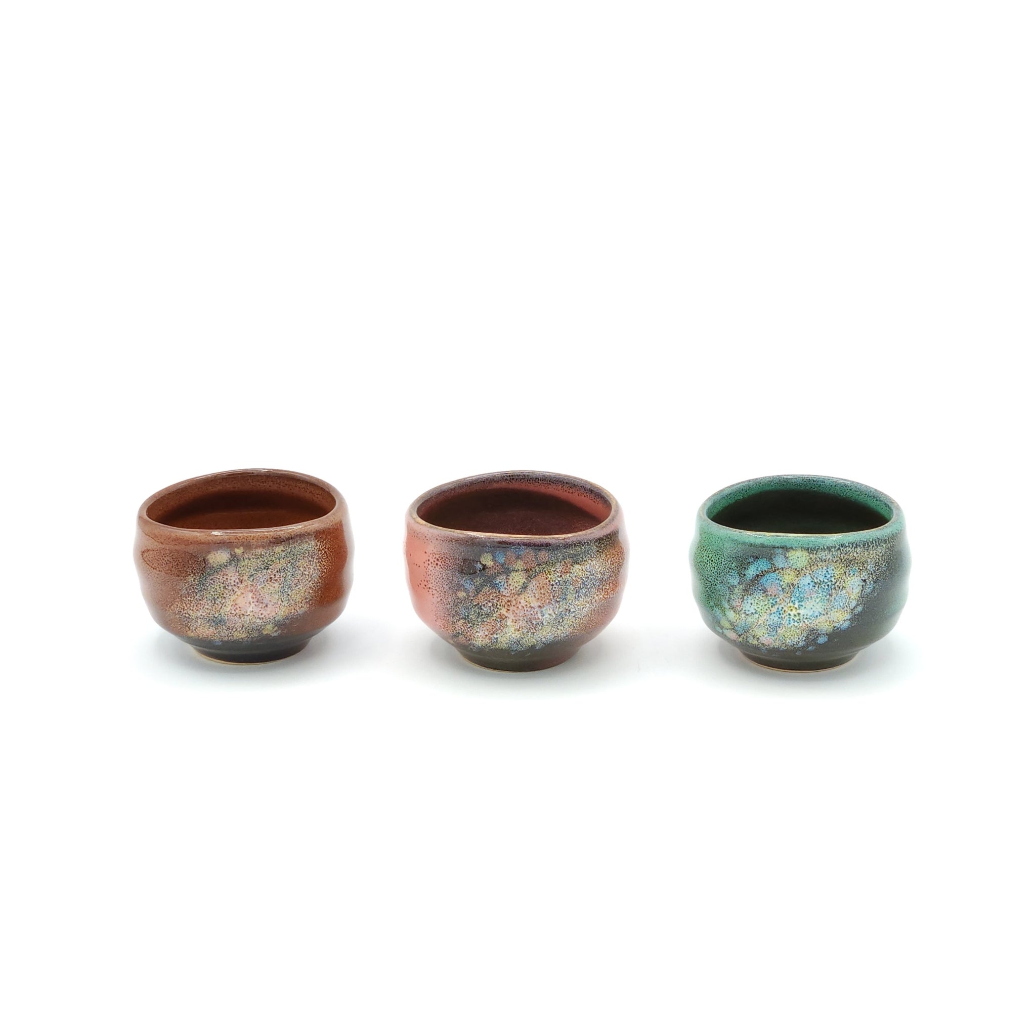 A set of three round Japanese ceramic sake cups in earthy brown, green and pink. Tsukushi
