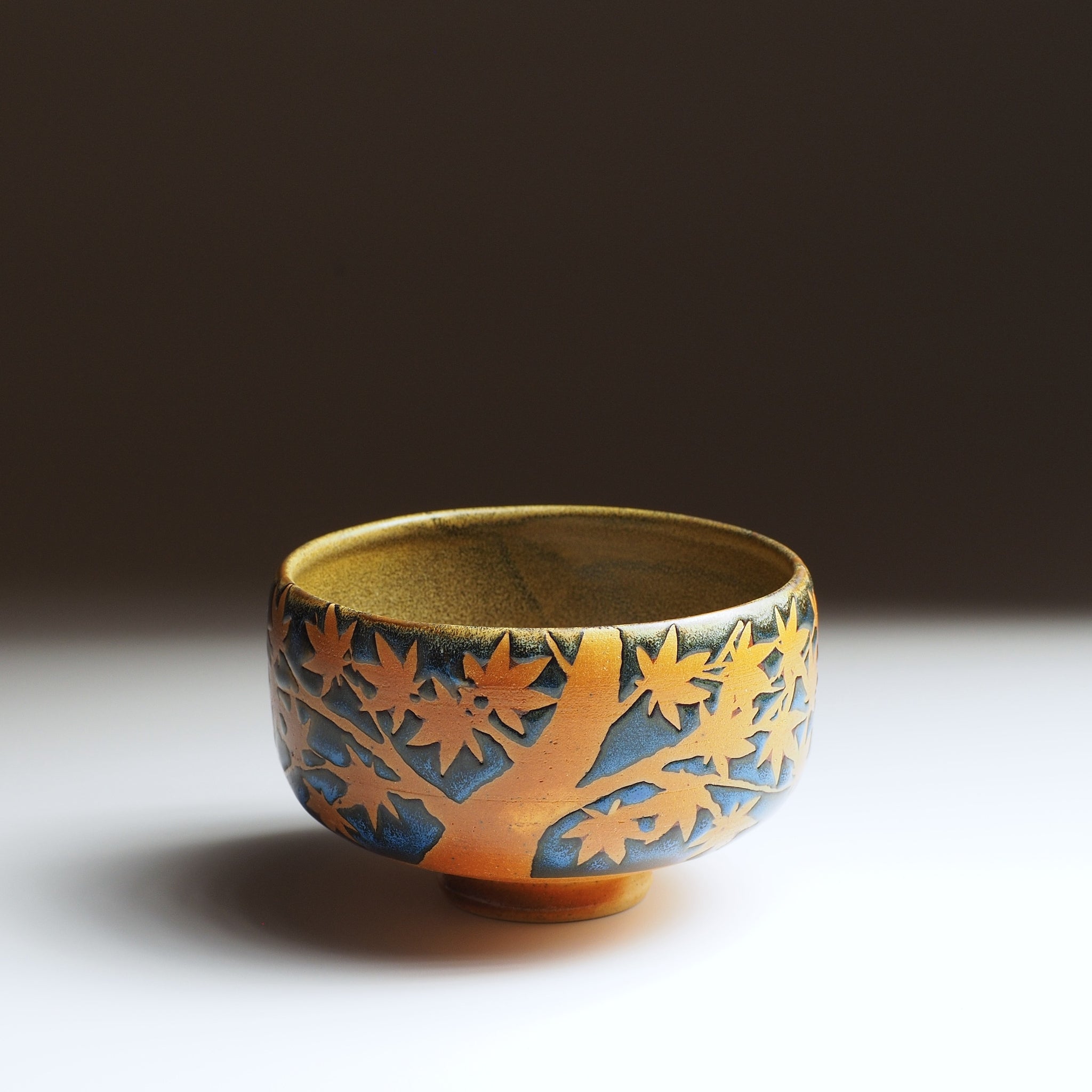 Front view of Soshu pottery matcha bowl with tree design on a gradient background