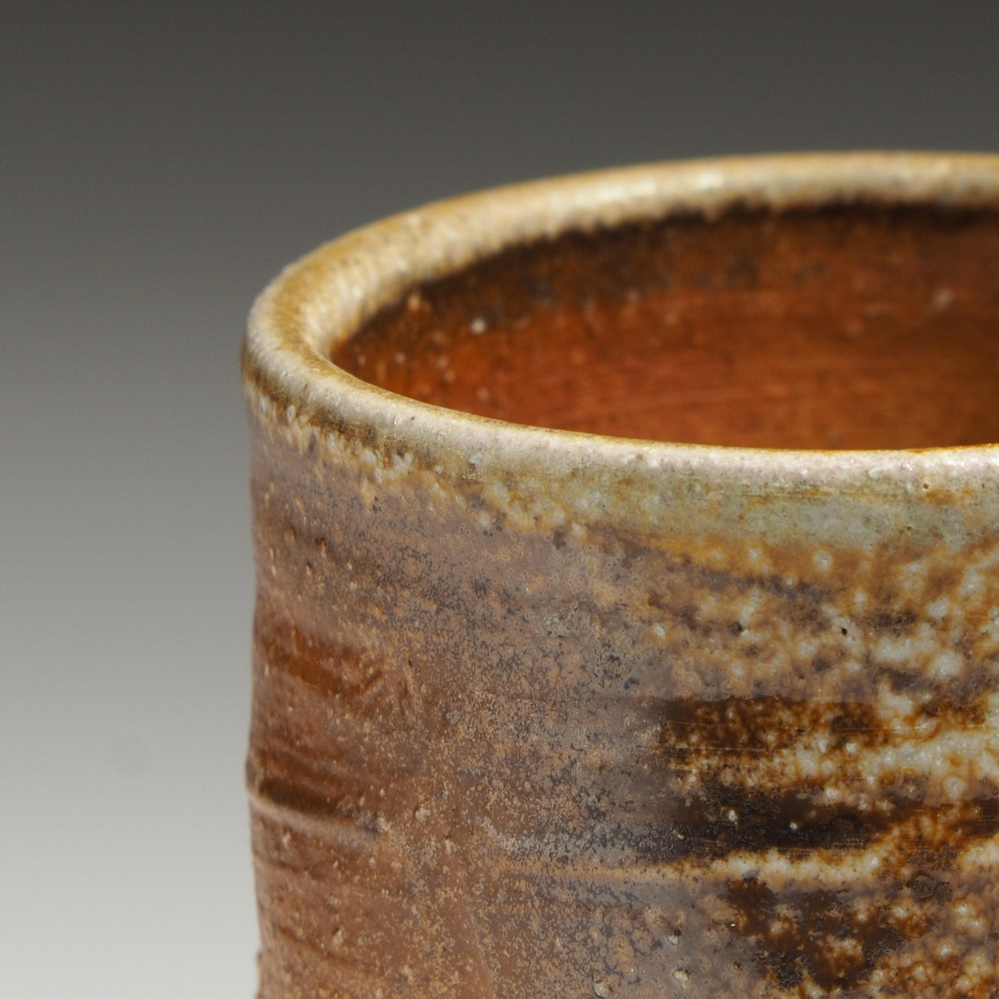 Close-up of a Yubae handmade Shigaraki yunomi showing its rim, dark interior, and textured brown surface.