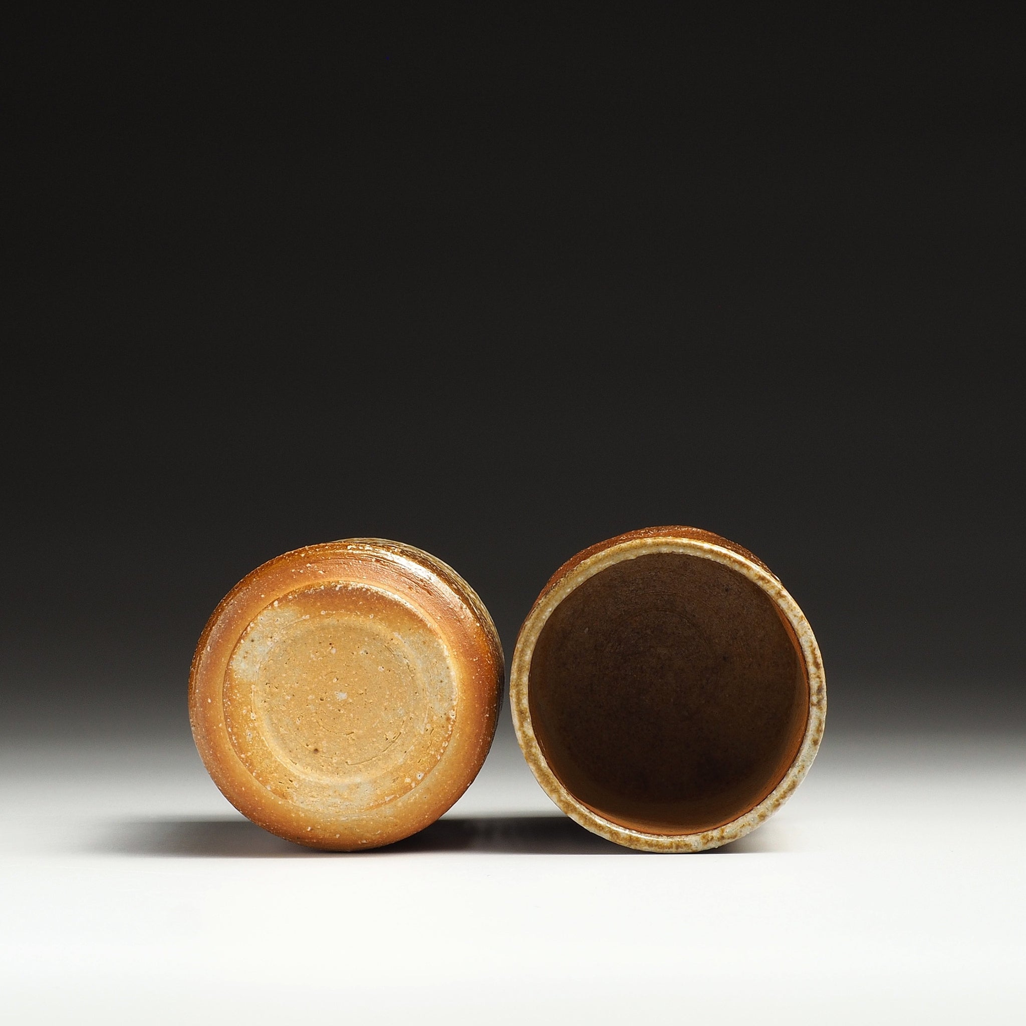 Yubae handmade Shigaraki yunomi set showing the base of one cup and the dark interior of the other.