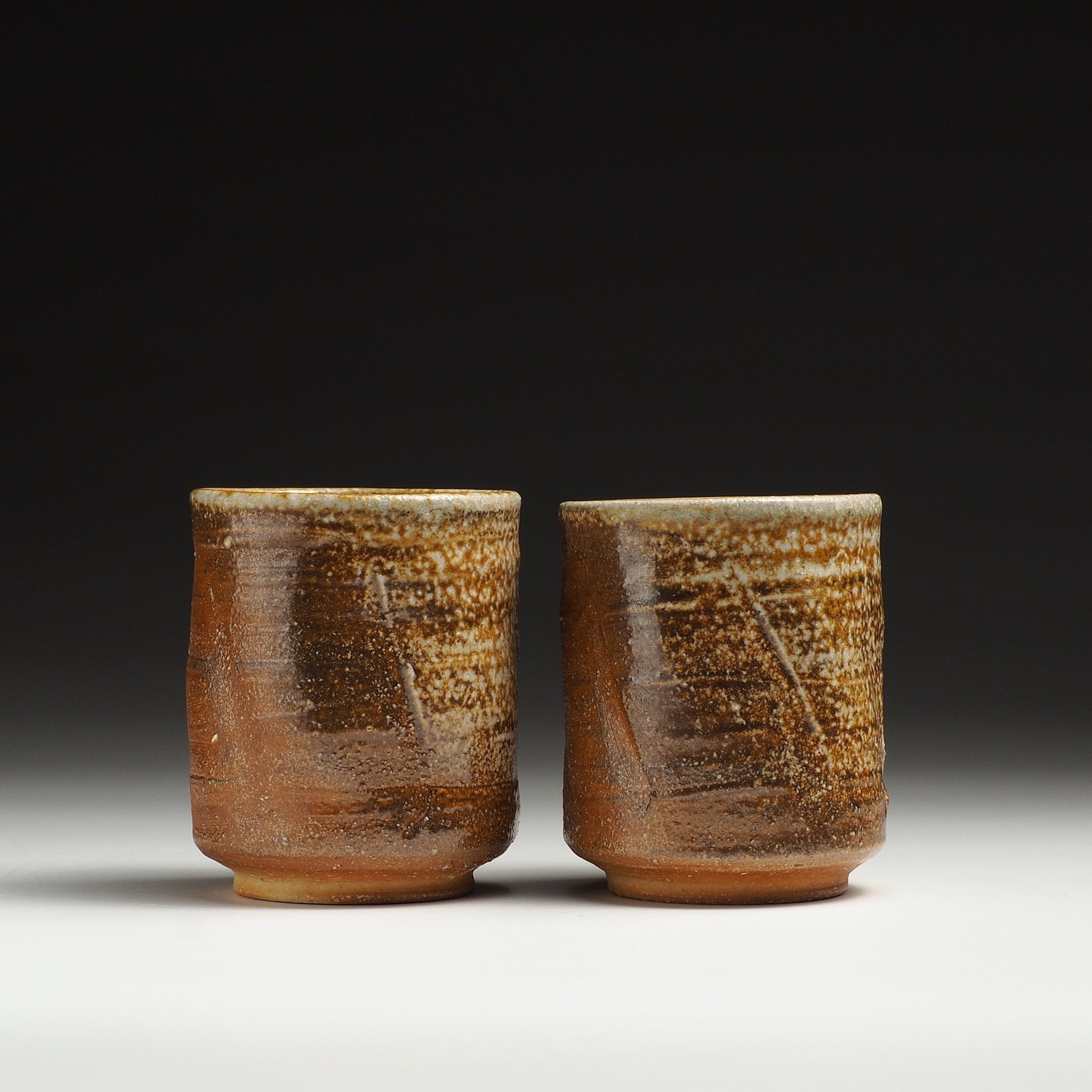 Front view of two Yubae handmade Shigaraki yunomi teacups showing their warm brown bodies and textured beige ash-fired surfaces.