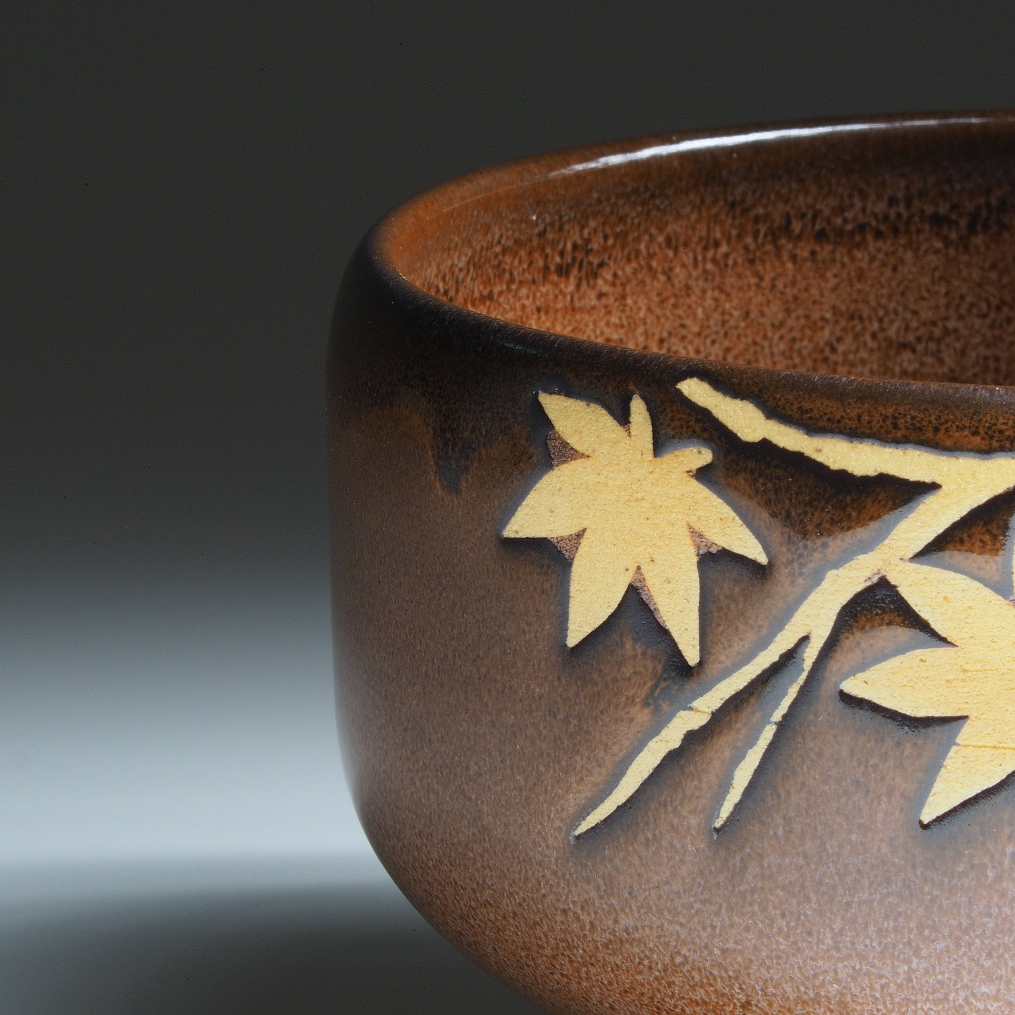 Close-up of Yūkaede matcha bowl, momiji maple leaves in natural clay against Nanasai Tenmoku brown glaze, Nunobiki Kiln