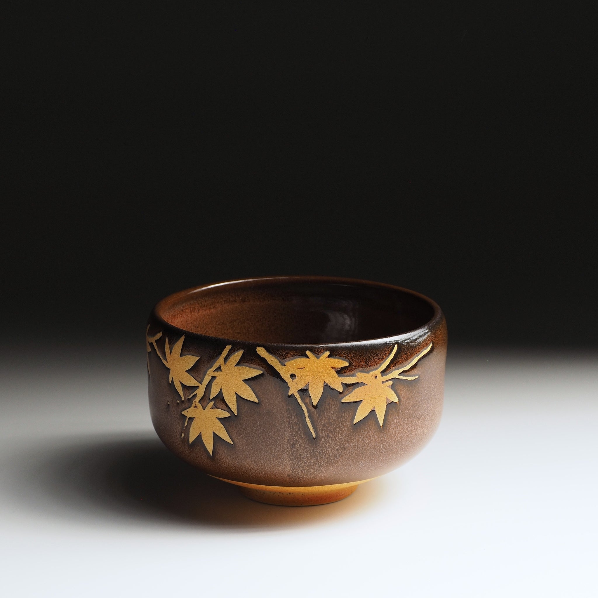 Yūkaede matcha bowl, angled view revealing open rim and momiji leaves spreading across Nanasai Tenmoku glaze, Nunobiki Kiln