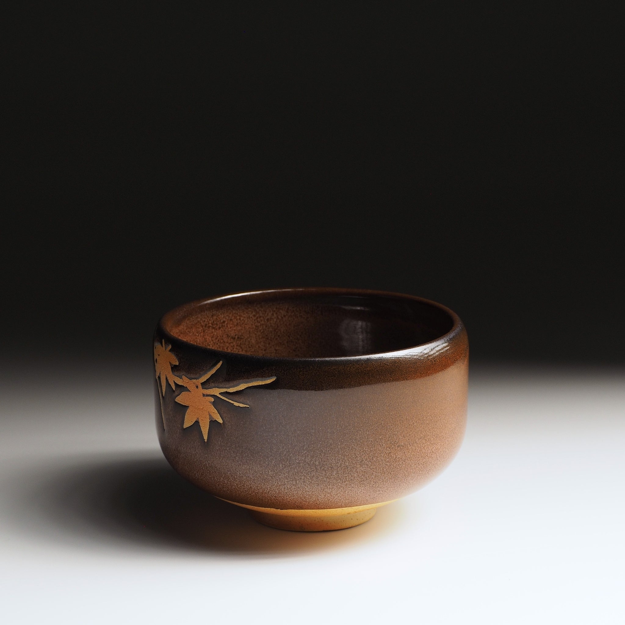 Yūkaede matcha bowl, three-quarter view showing glaze depth and delicate momiji sprig in negative-space clay, Nunobiki Kiln