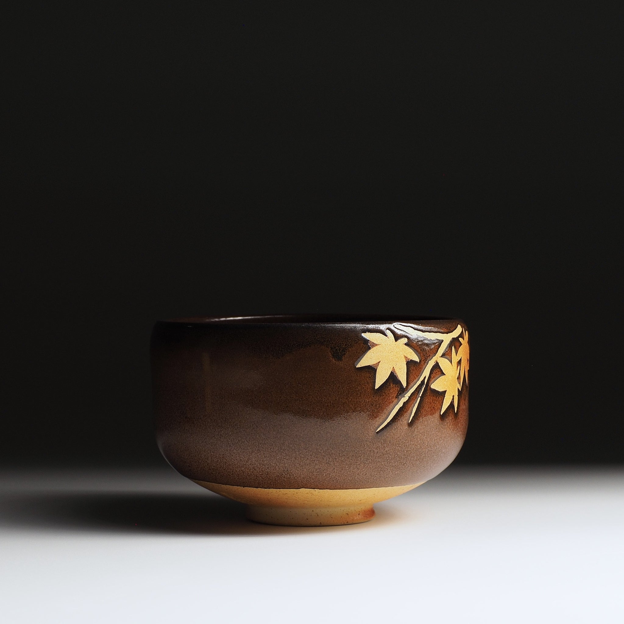 Yūkaede matcha bowl, clean side profile with momiji branch emerging at rim, warm clay foot, Nunobiki Kiln, Japan