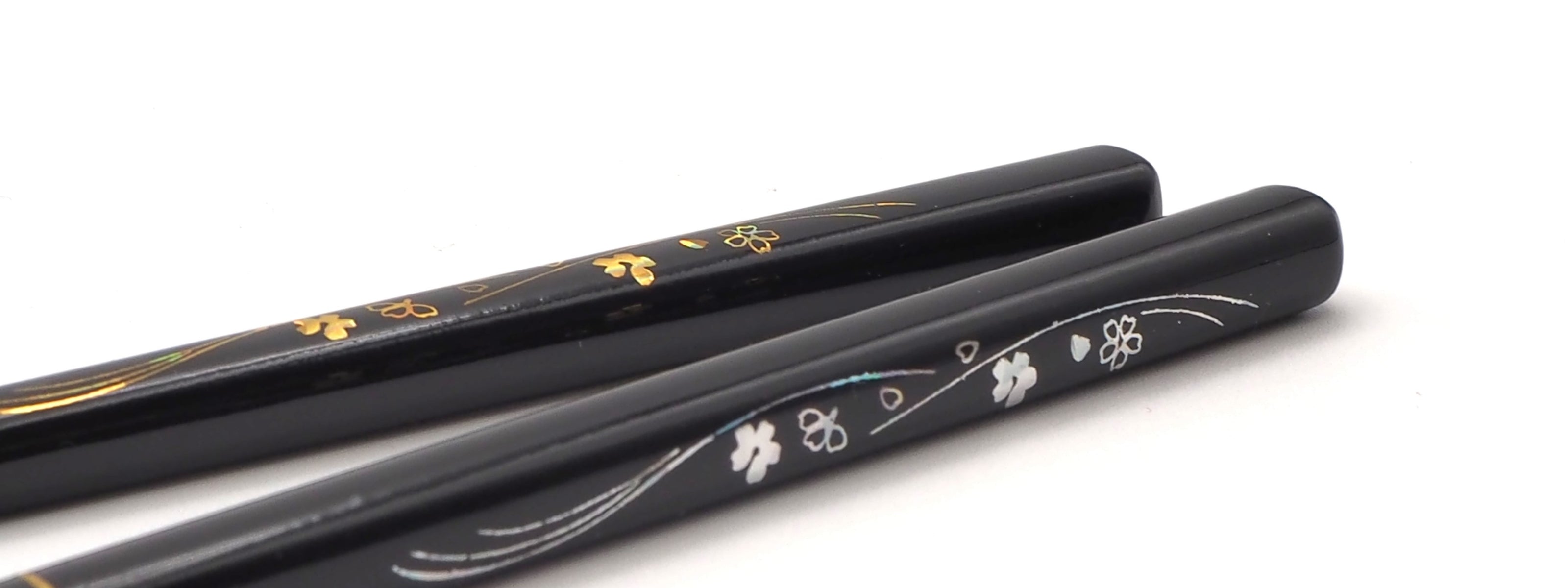 Two black lacquered Japanese wooden chopsticks, decorated with gold and white floral inlays, shown on a plain white background.