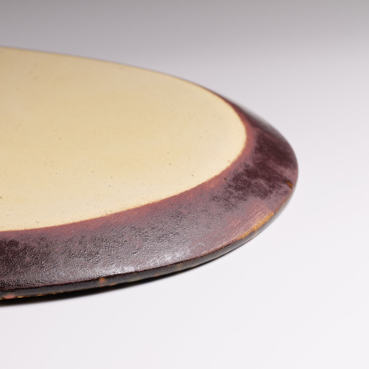 Macro photograph of the Hanami ceramic plate underside, showing its cream-colored surface, dark brown rim, and subtle handmade texture.