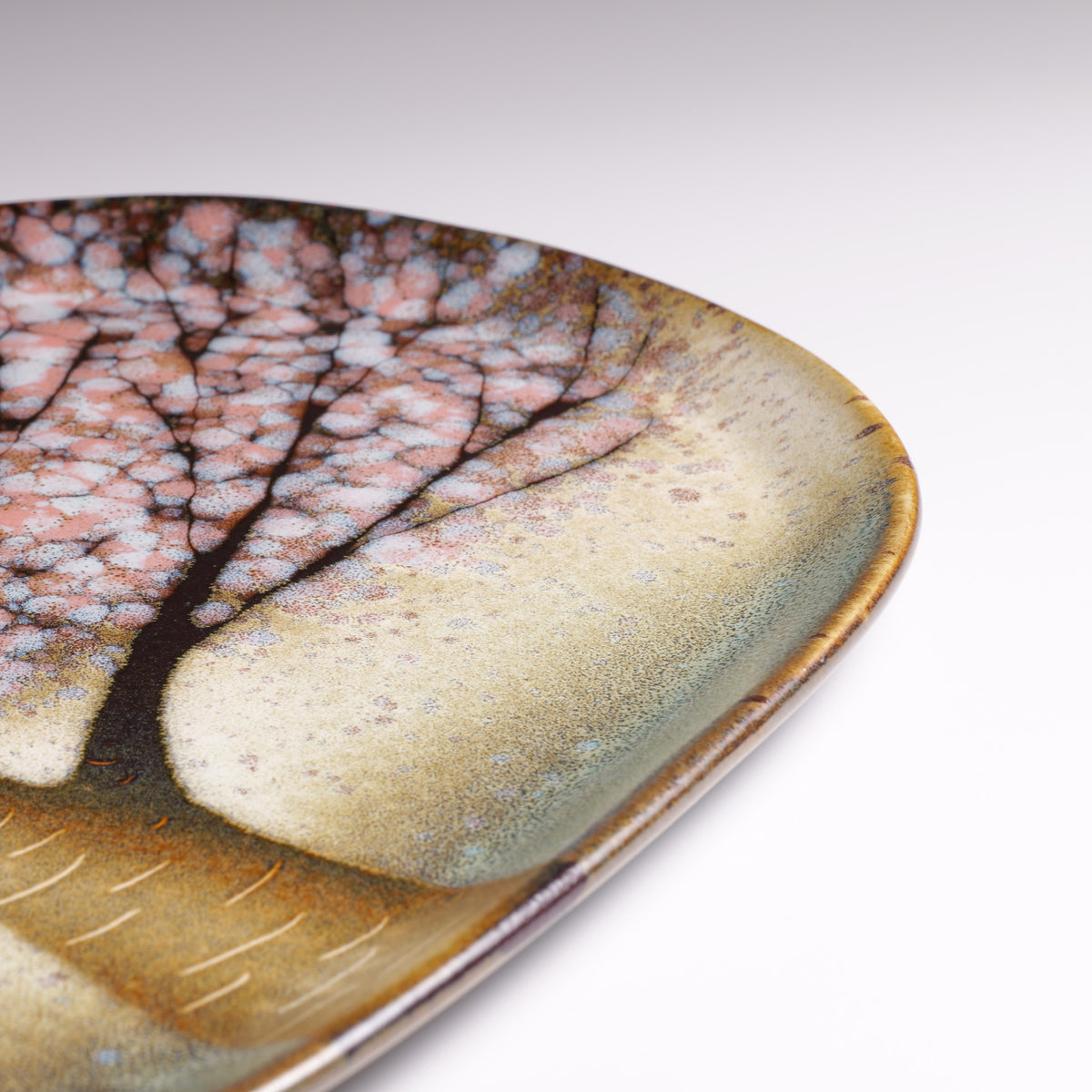 Close-up of the Hanami handmade Japanese ceramic plate, featuring pink sakura blossoms, dark branches, and textured green and golden glaze.