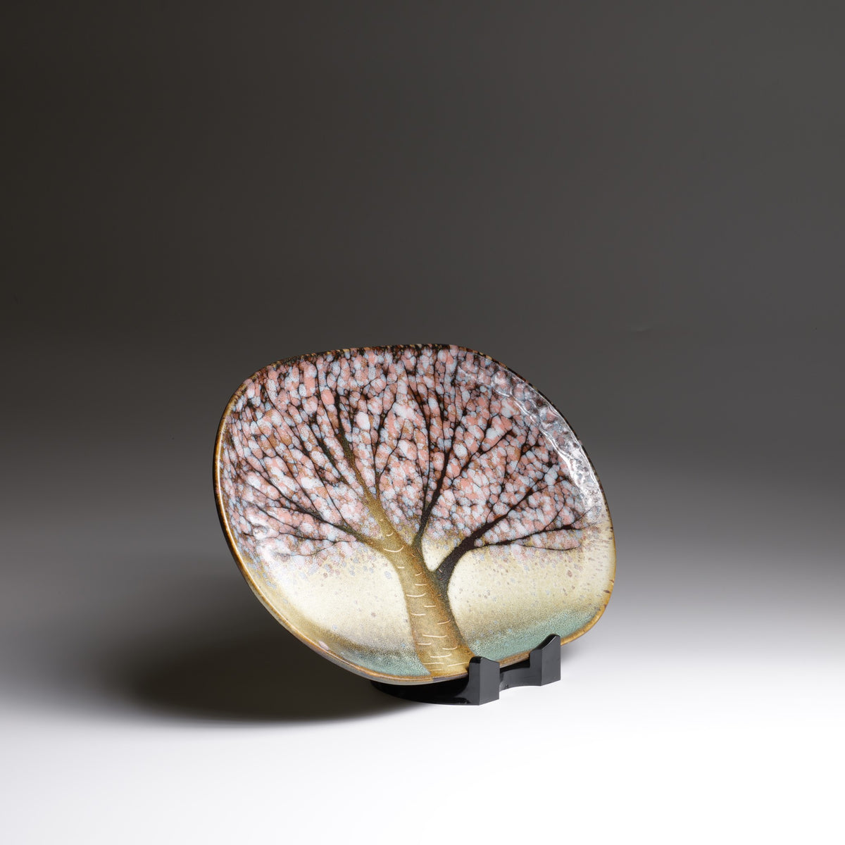 Hanami Japanese ceramic plate displayed upright on a black stand, highlighting its rounded rectangular shape and cherry blossom tree motif.