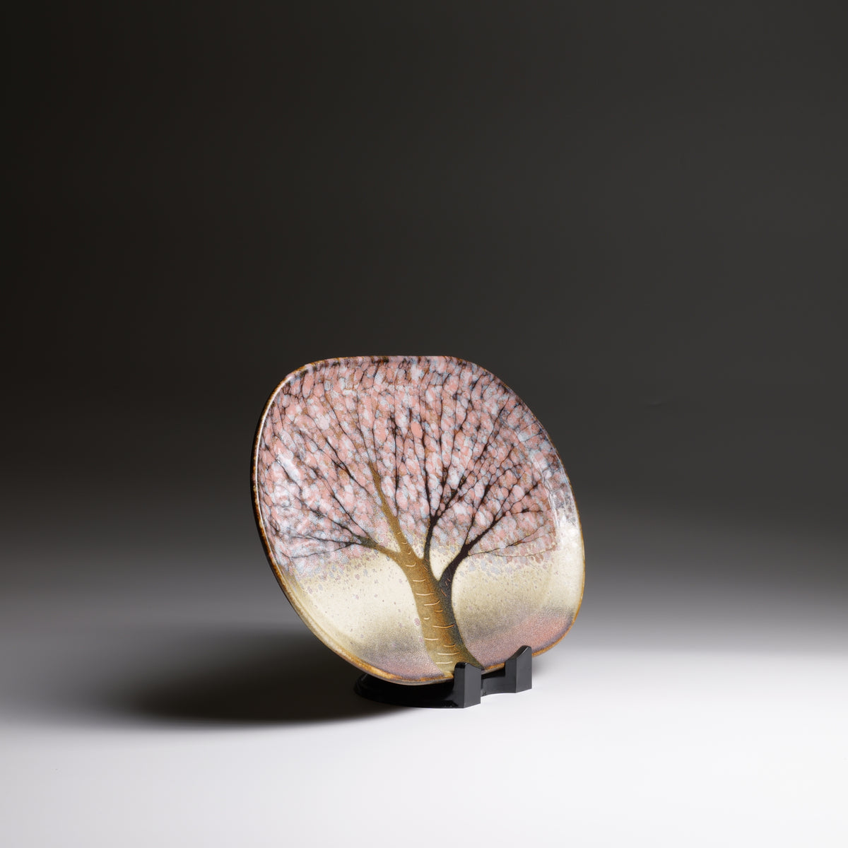 Japanese handmade ceramic plate with cherry blossoms decorations and pink shades on a stand.